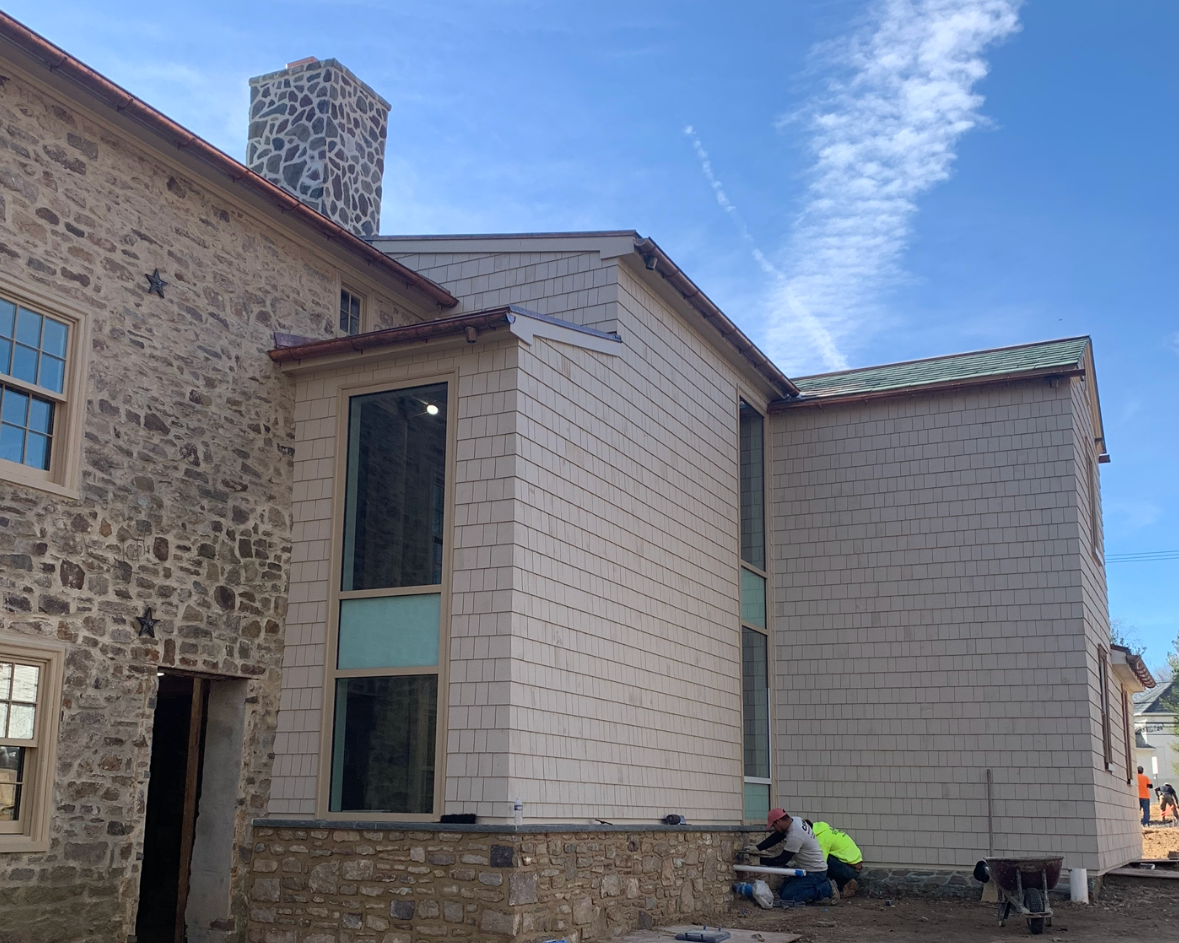 Construction workers installing siding on a house with stone and beige shingle exterior under a blue sky.
