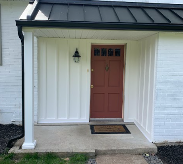 Front porch with a brown door, black lantern light, and white paneling on the porch walls