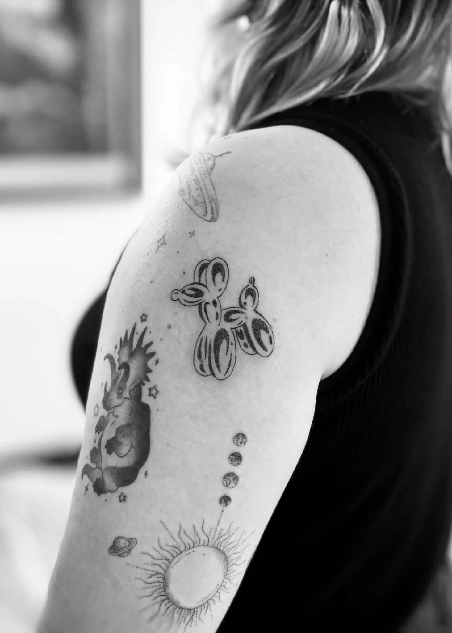 Close-up of a person's arm with various black and white tattoos, including a butterfly, sun, planets, and celestial designs.