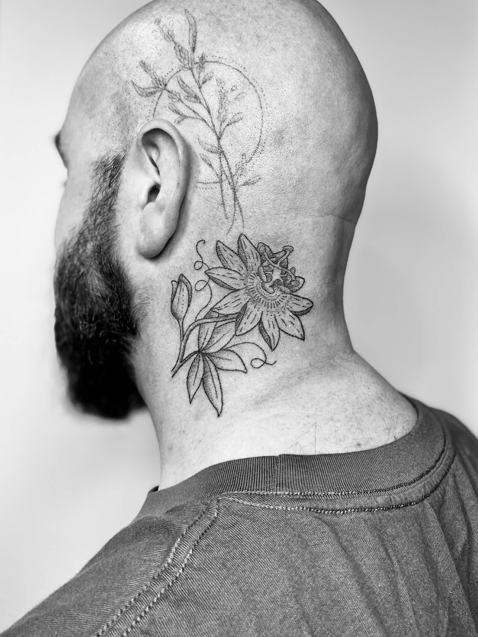 A man with a beard and a shaved head, showing tattoos on his head and neck, one of a tree and another of a large flower with leaves.
