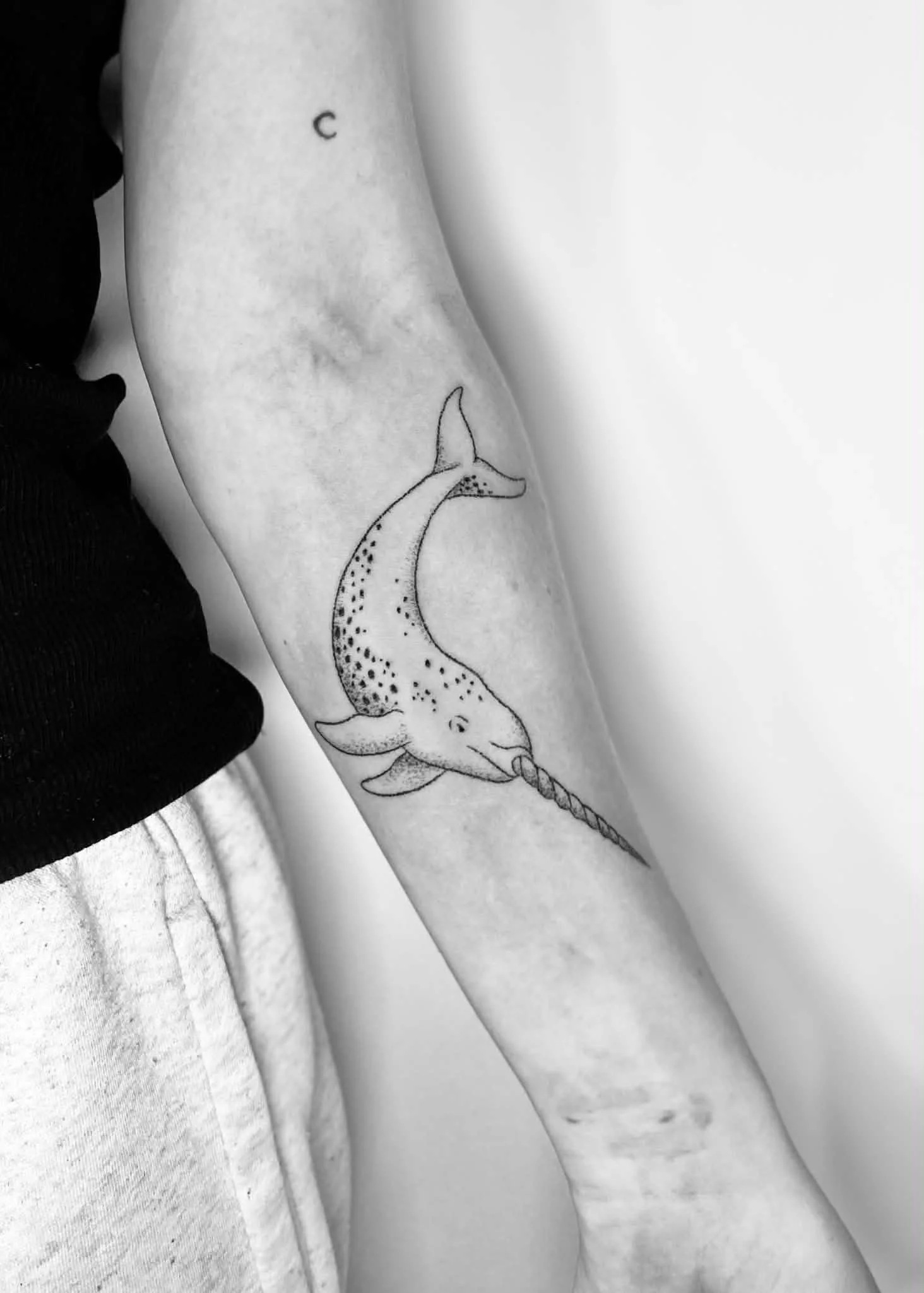 Tattoo of a narwhal on a person's arm in black and white.