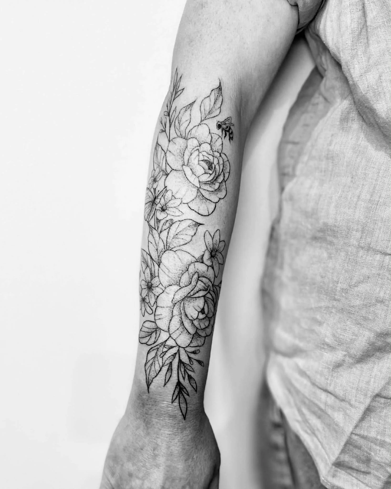 A black and white photograph of a person's arm with a floral tattoo, including roses and leaves.