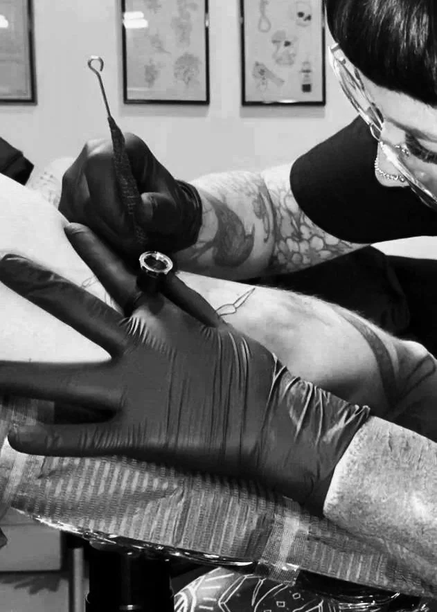 A person getting a tattoo on their arm from a tattoo artist in a tattoo shop.