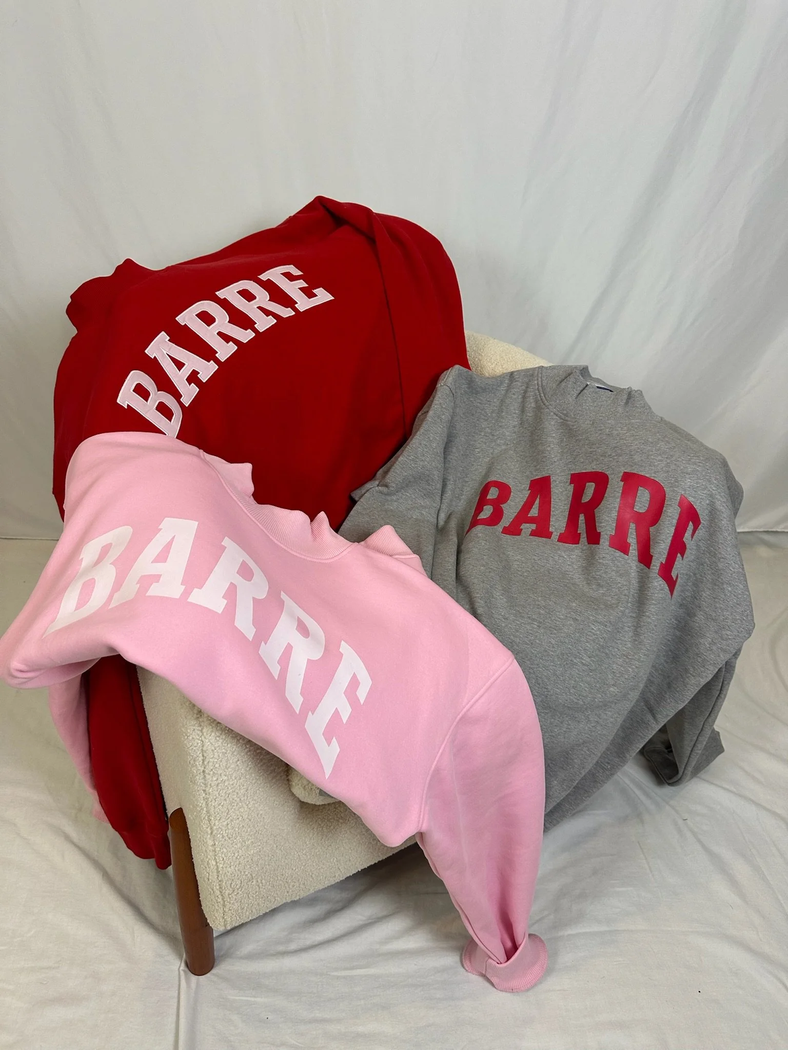 Colorful sweatshirt and hoodie with the word 'BARRF' on a beige chair against a white background.