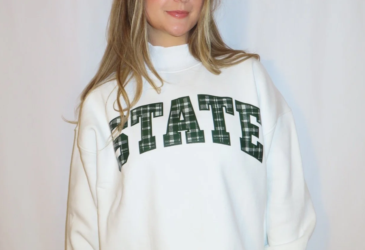 A woman wearing a white sweatshirt with the word "STATE" printed on the front in plaid pattern.