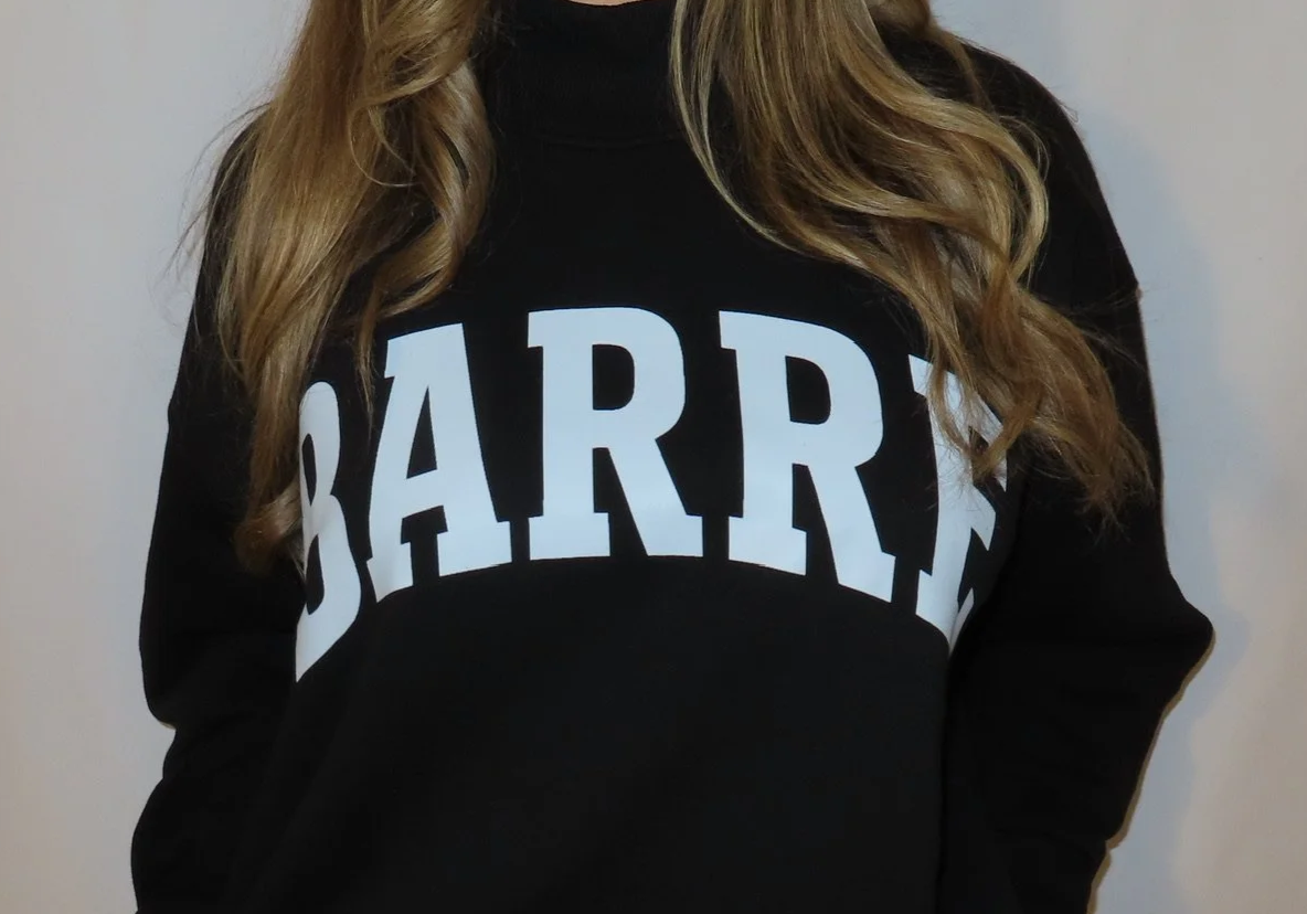 A person with long, wavy blonde hair wearing a black sweatshirt with large white text that spells 'BARRRE' across the front.