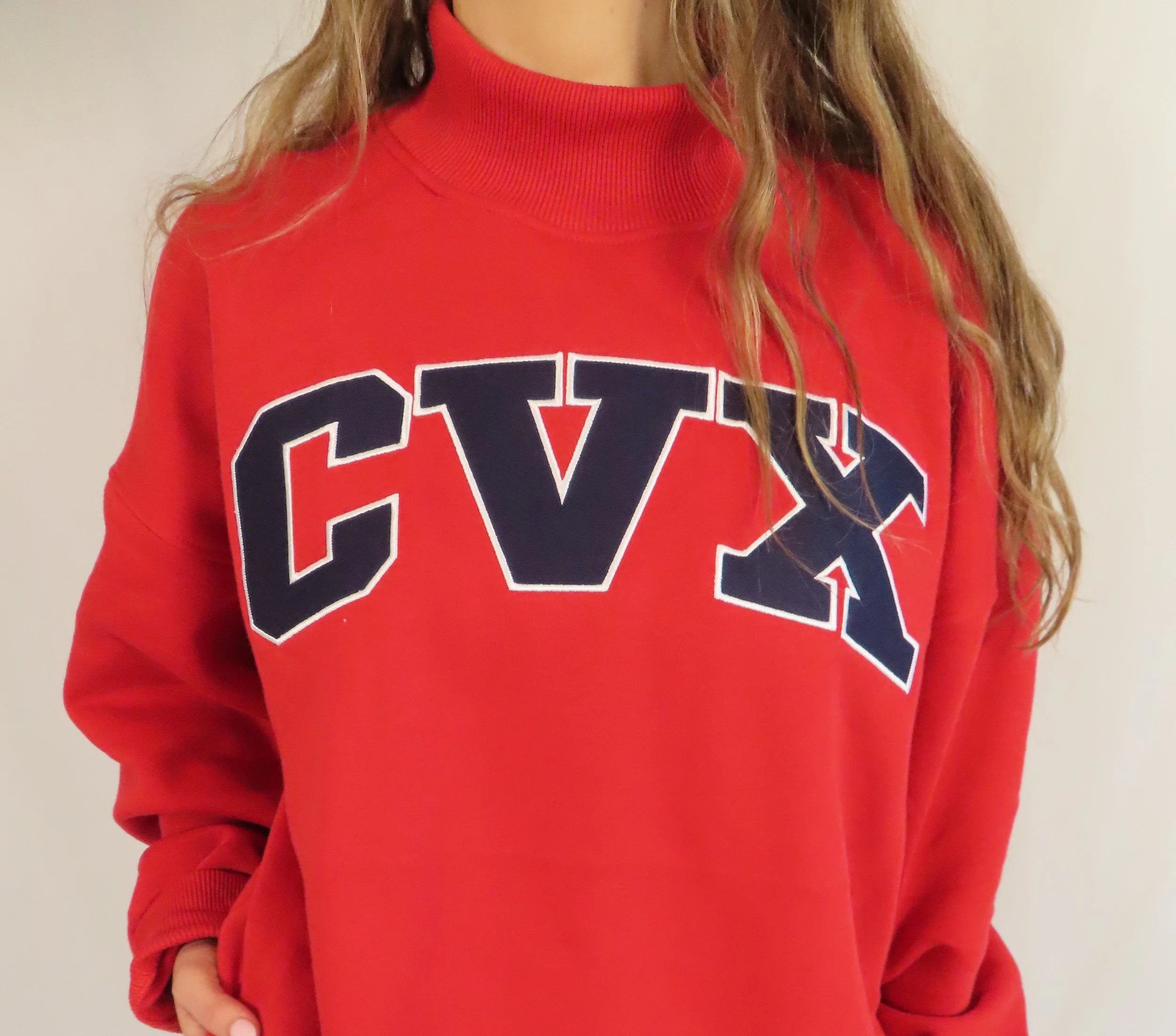 A person wearing a red sweatshirt with large navy and white letters on the front, standing against a plain light-colored background.