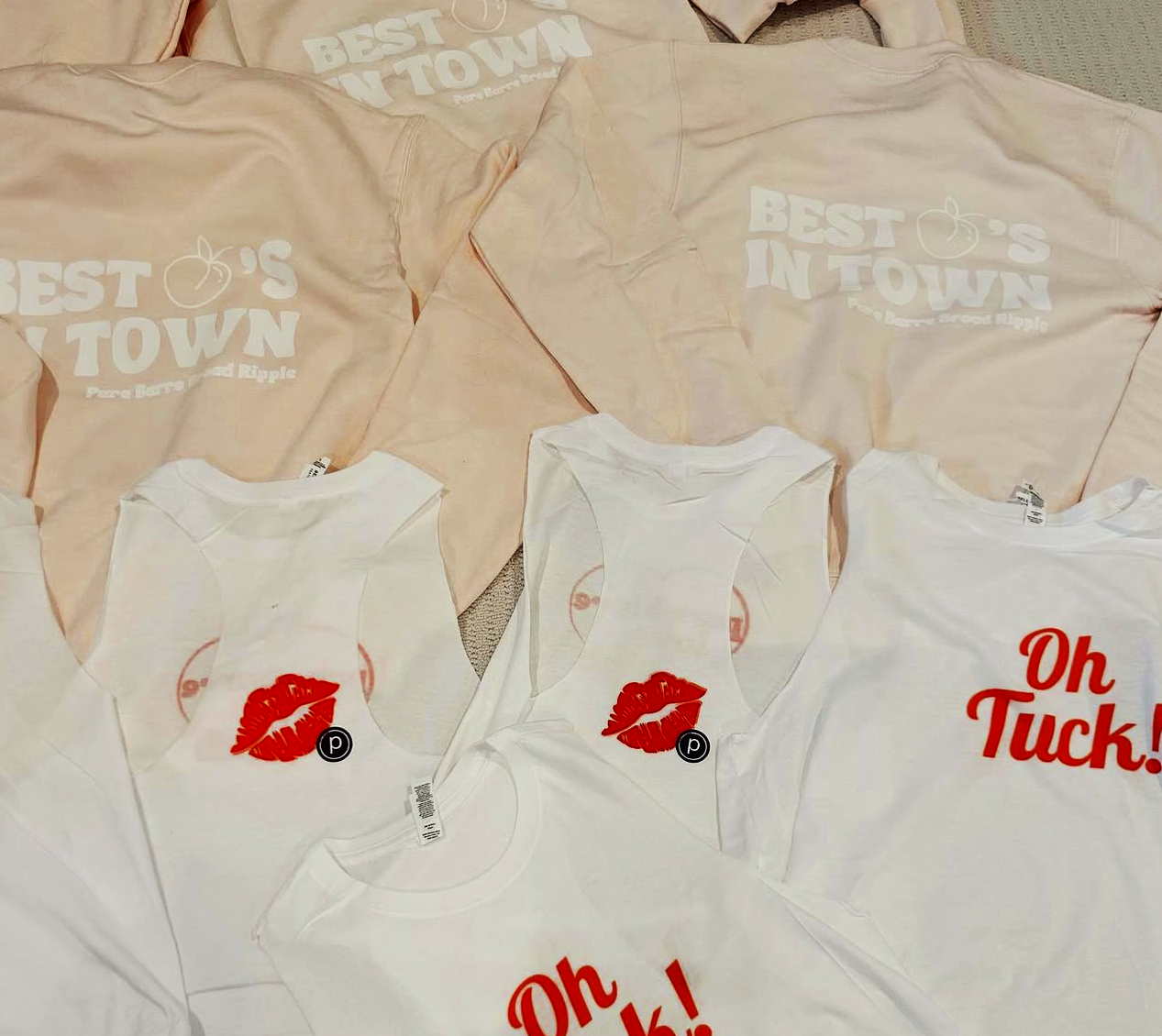 Collection of pink and white T-shirts and tank tops with various printed designs, some featuring red lip print and text like "Oh Tuck!" and "Best O's in Town."