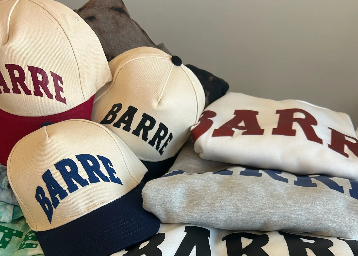 Collection of baseball caps and folded T-shirts with the word 'BARRÉ' printed on them in different colors.