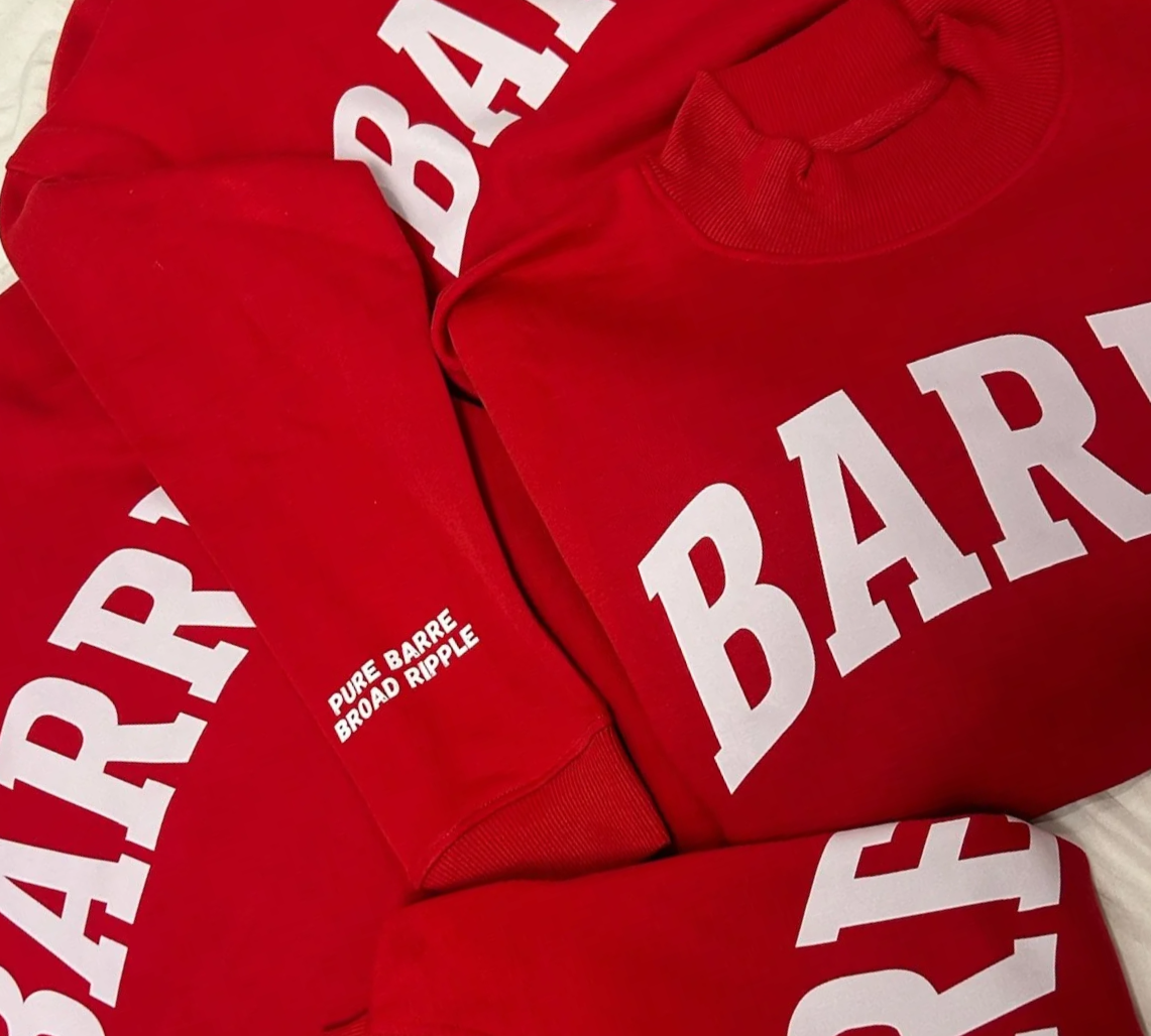 Red sweatshirts with white text that says 'PURE BARRE BROAD RIPPLE' and large white letters spelling 'BARRE'.