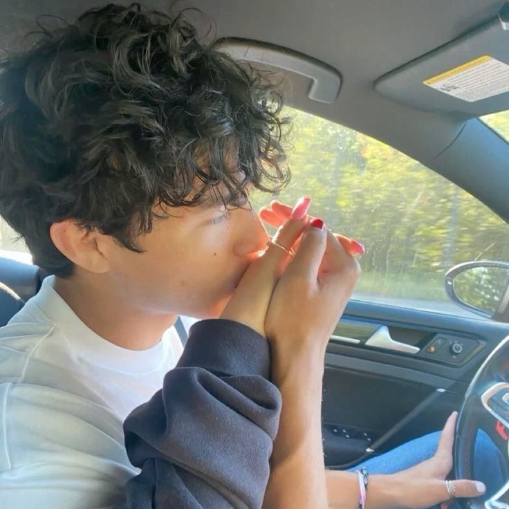 Young woman with curly hair sitting in a car, cupping her hands over her nose in a peaceful moment while on a road trip.