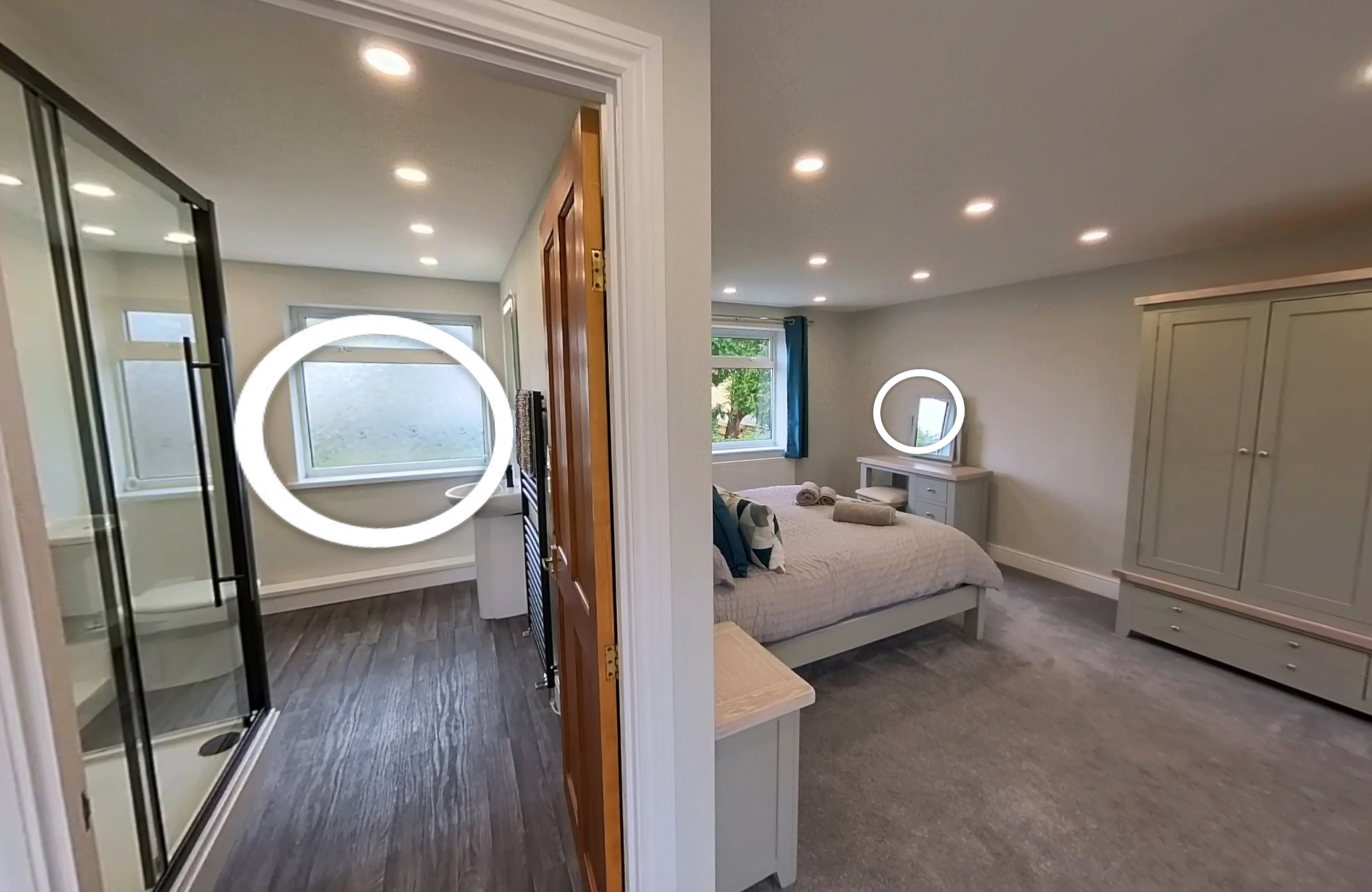 A split view of two bedrooms: the left side shows a bathroom with a shower, a frosted window, and recessed ceiling lights; the right side displays a bedroom with a bed, vanity table with mirror, window with blue curtains, and a large wardrobe, all with recessed ceiling lights.