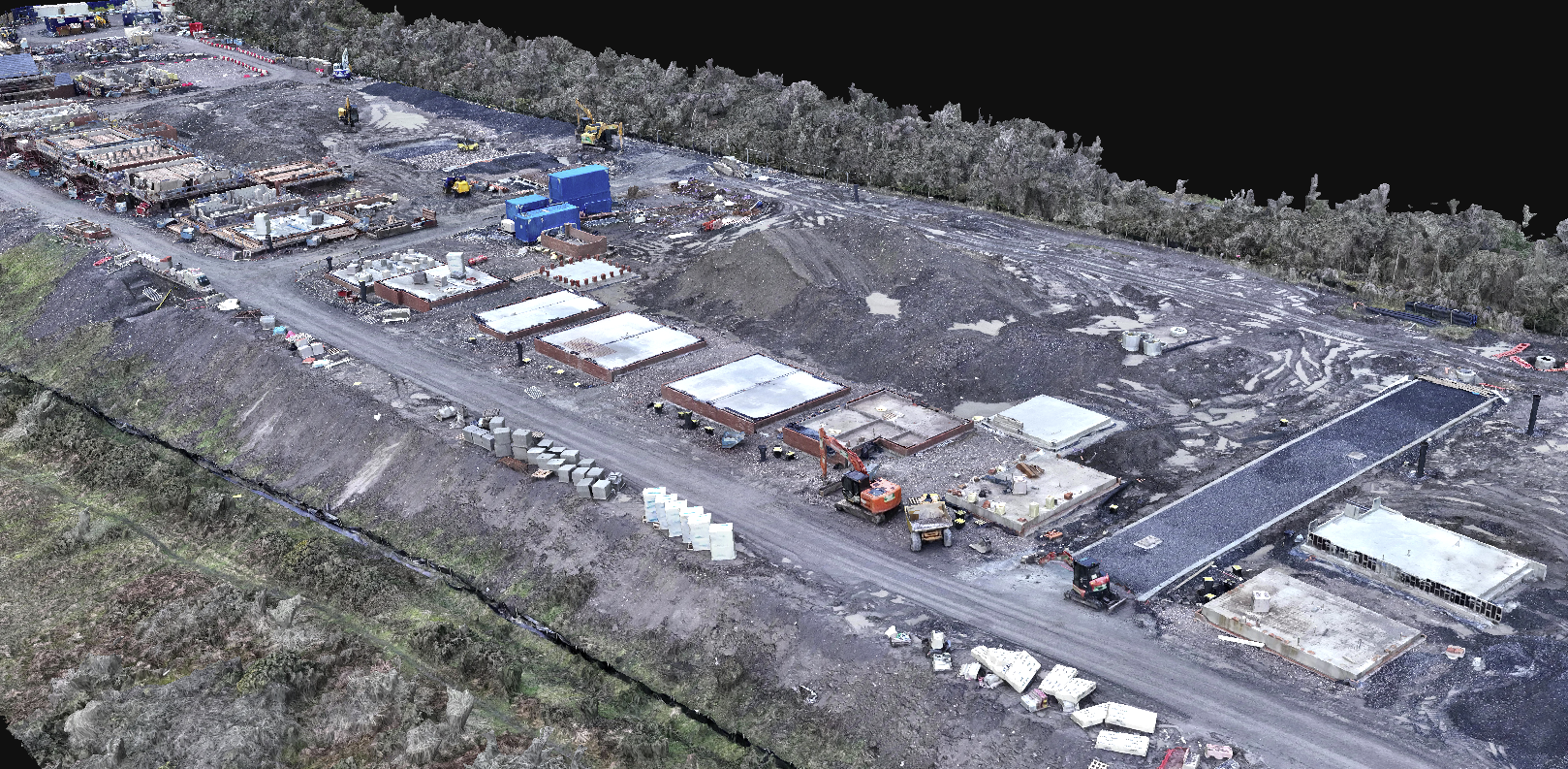 An aerial view of a construction site with partially built structures, construction equipment, and materials, surrounded by excavation areas and greenery.