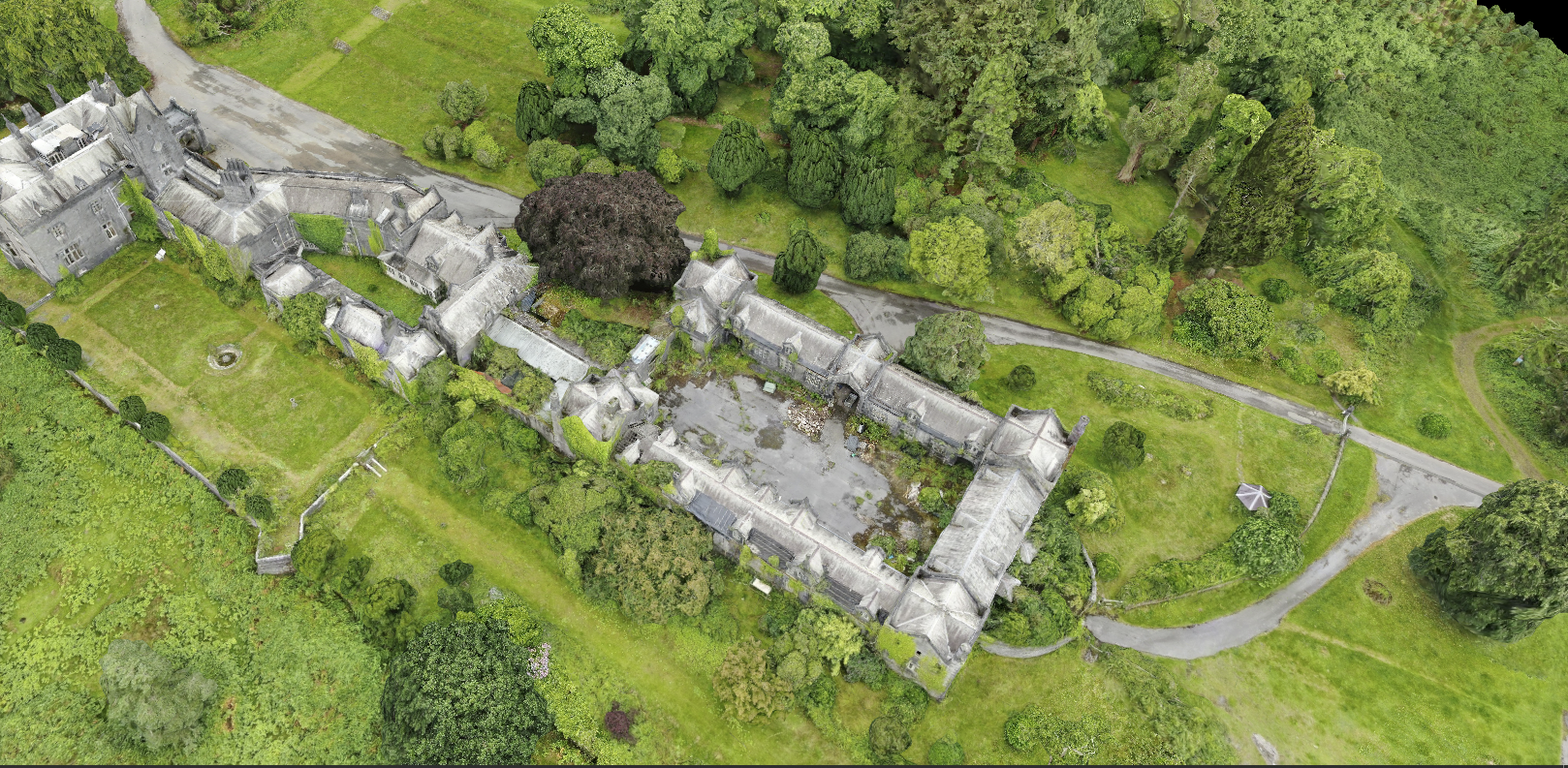 Aerial view of an old castle with grey stone walls surrounded by green lawns, trees, and pathways.