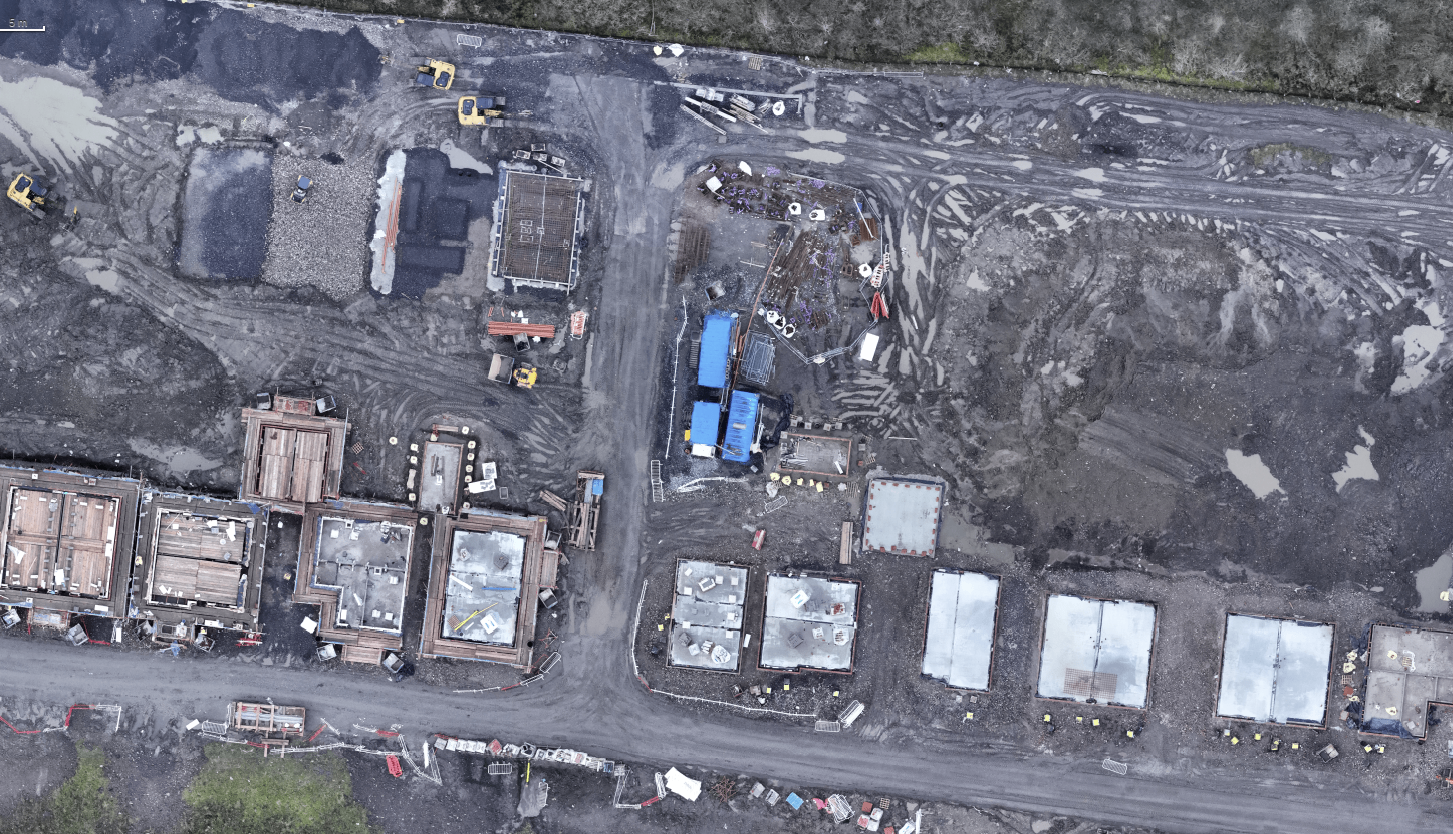 Aerial view of a construction site with multiple buildings in progress, construction equipment, and muddy ground.