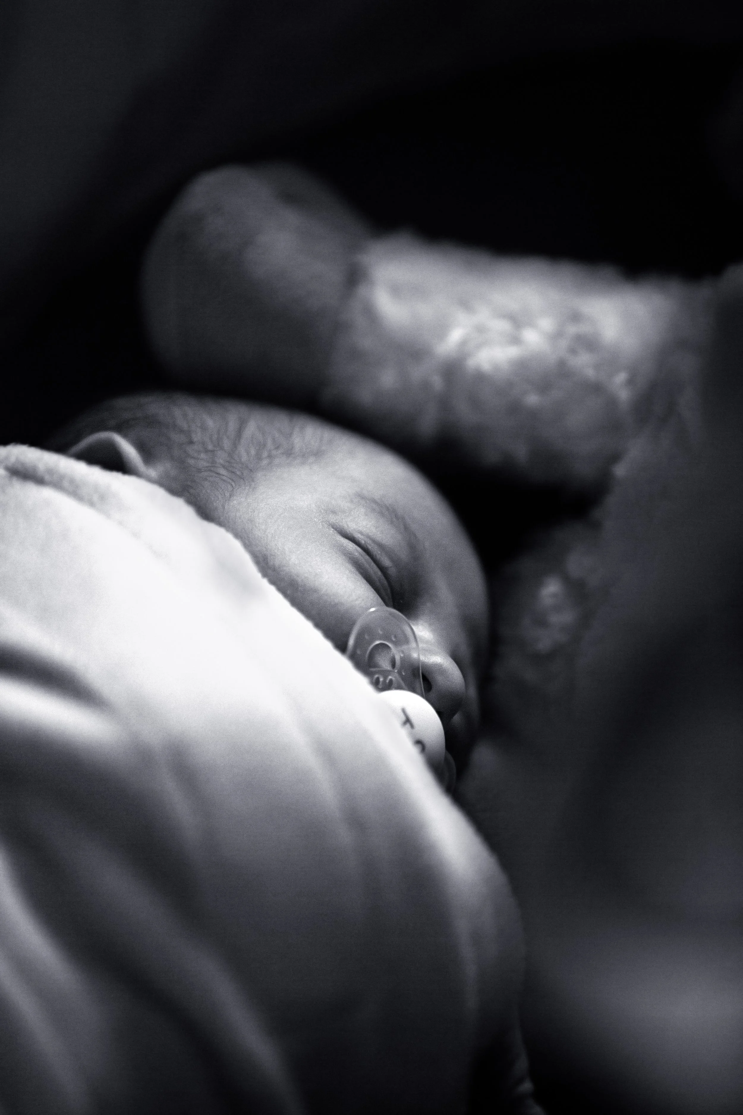 Black and white photo of a sleeping baby with a pacifier, resting on a soft blanket.