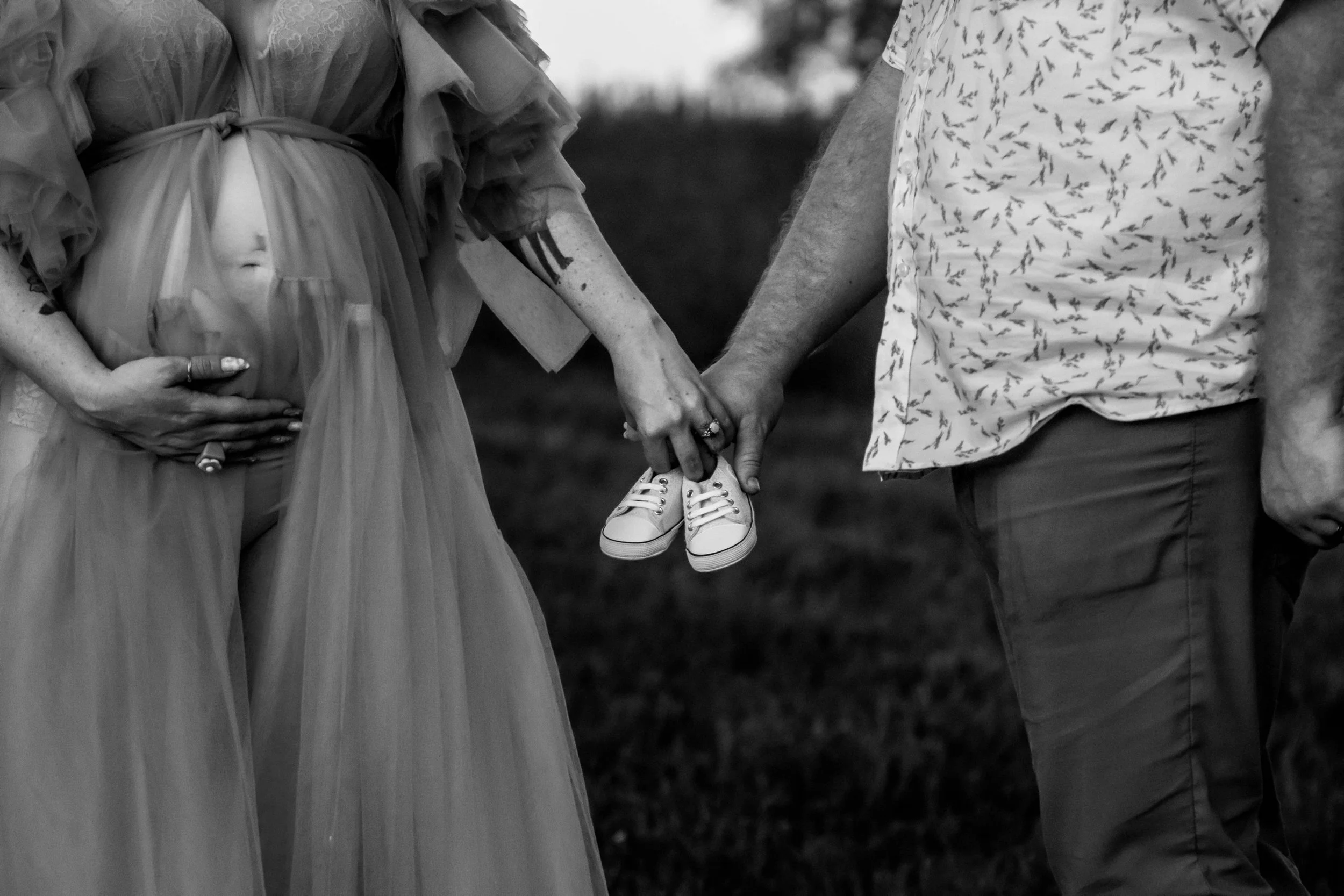 A pregnant woman and a man holding hands, with the woman holding a pair of tiny baby shoes.