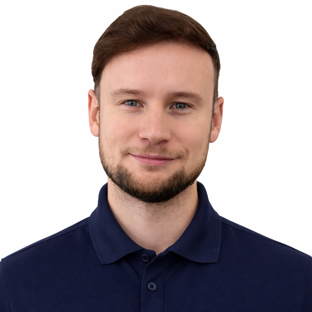 A young man with brown hair and a beard, wearing a navy blue collared shirt, smiling against a white background.