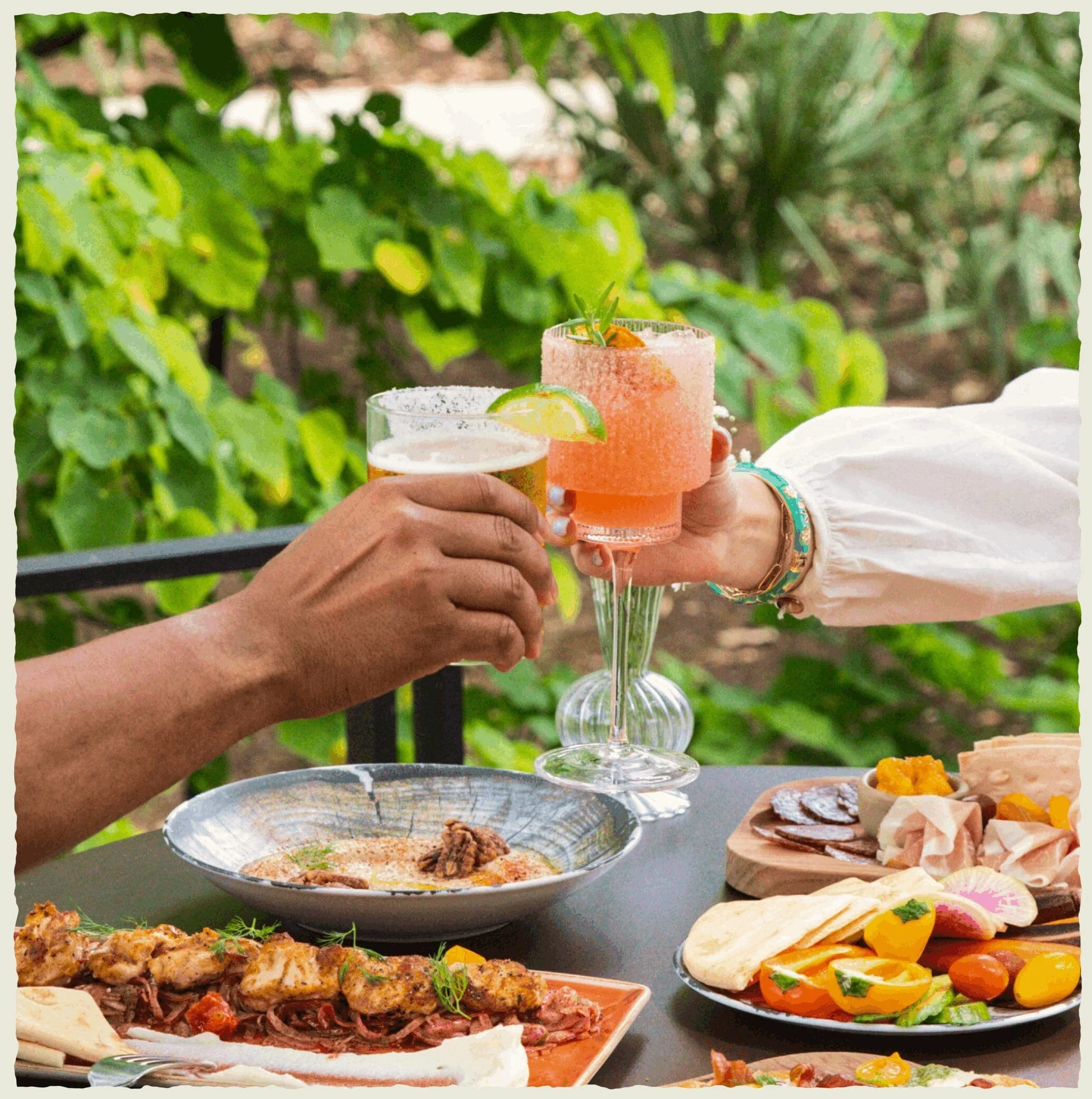 two people giving cheers with a margarita and pink cocktail over an artful meal