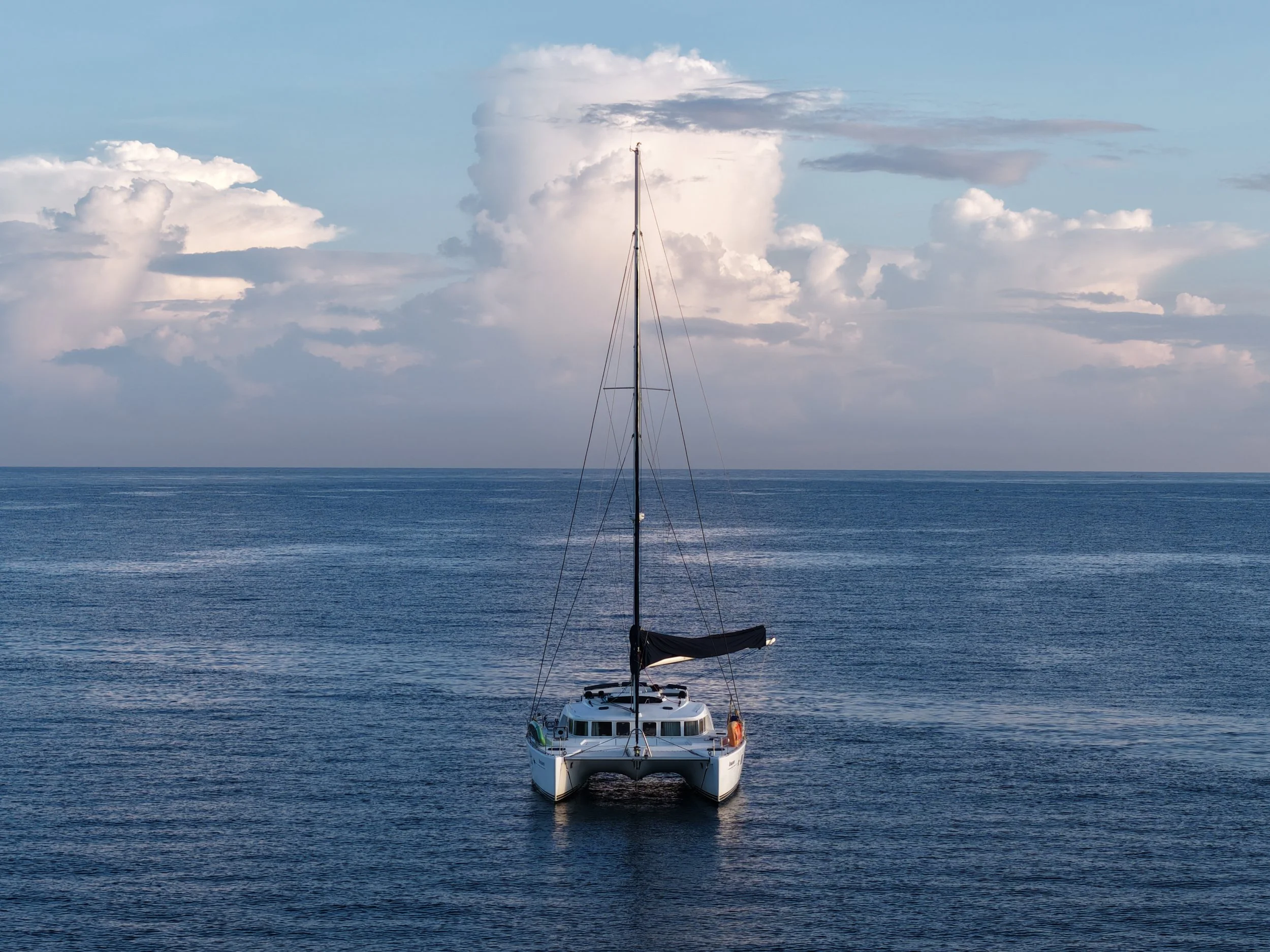 A sailboat floating on calm ocean waters under a cloudy sky