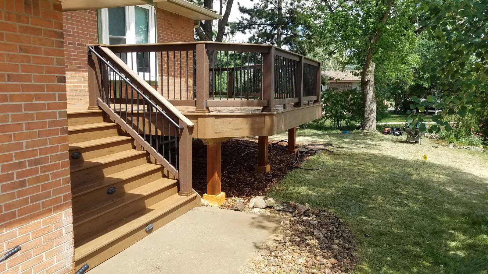 A newly constructed composite deck with stairs attached to a brick house, surrounded by a backyard with trees and grass.