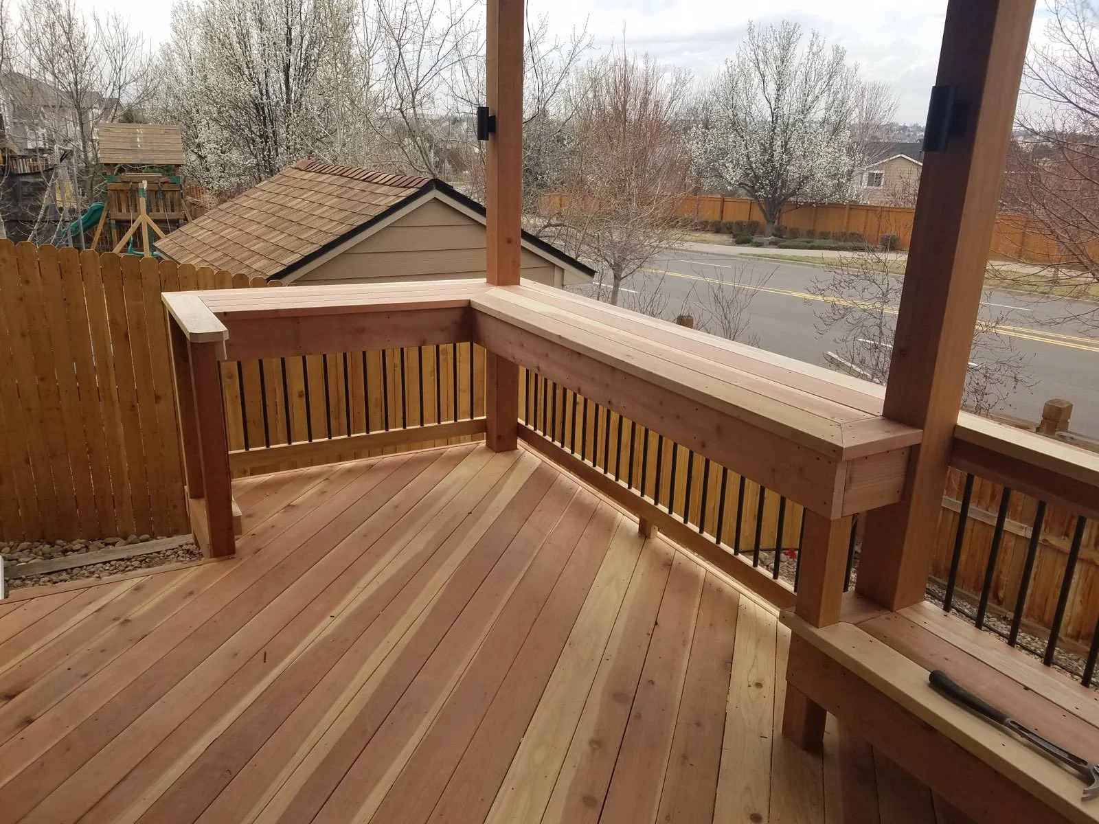 Freshly built wooden porch with railing, overlooking a suburban neighborhood street and trees.
