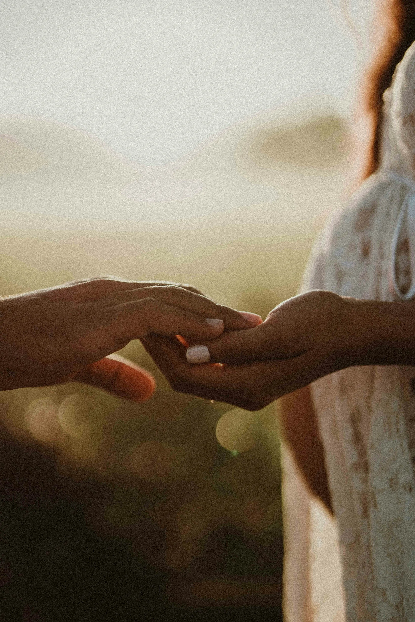 Close-up of two hands gently touching, outdoors with a blurred background and warm sunlight.