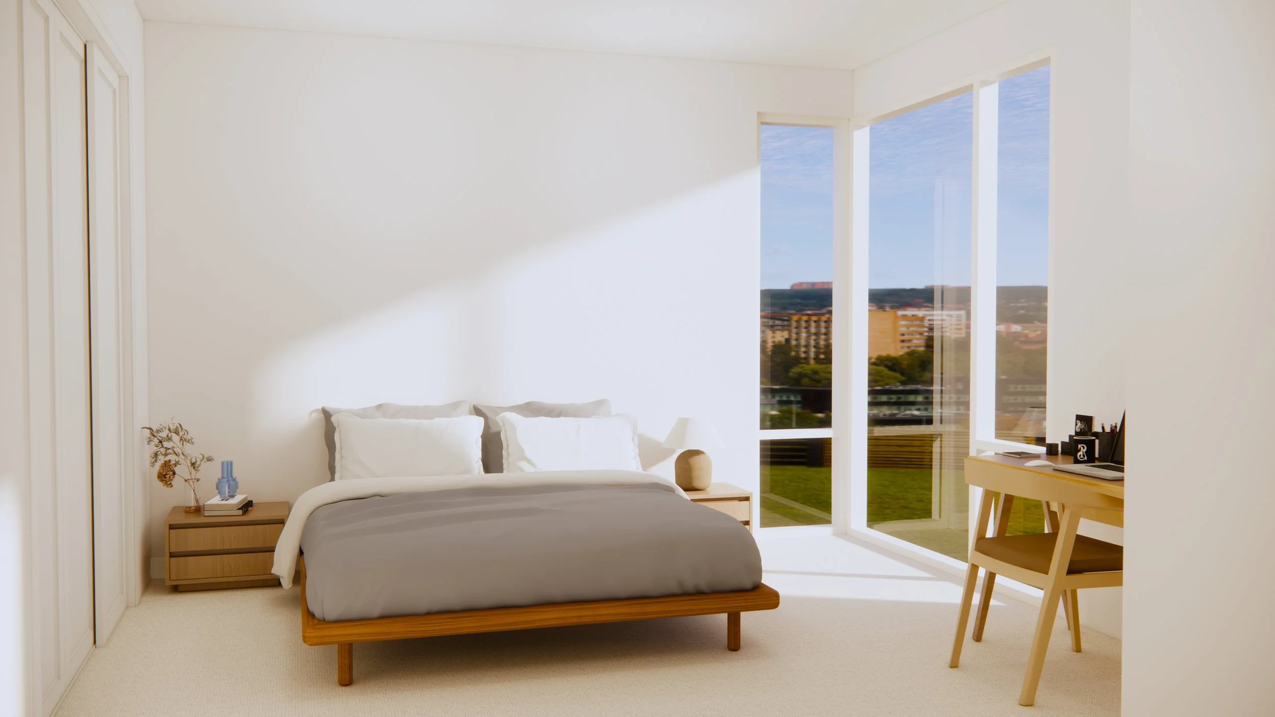 Bright bedroom with white walls, large window showing cityscape, bed with gray bedding, wooden nightstand with decorative items, desk with a chair, and minimal decor.