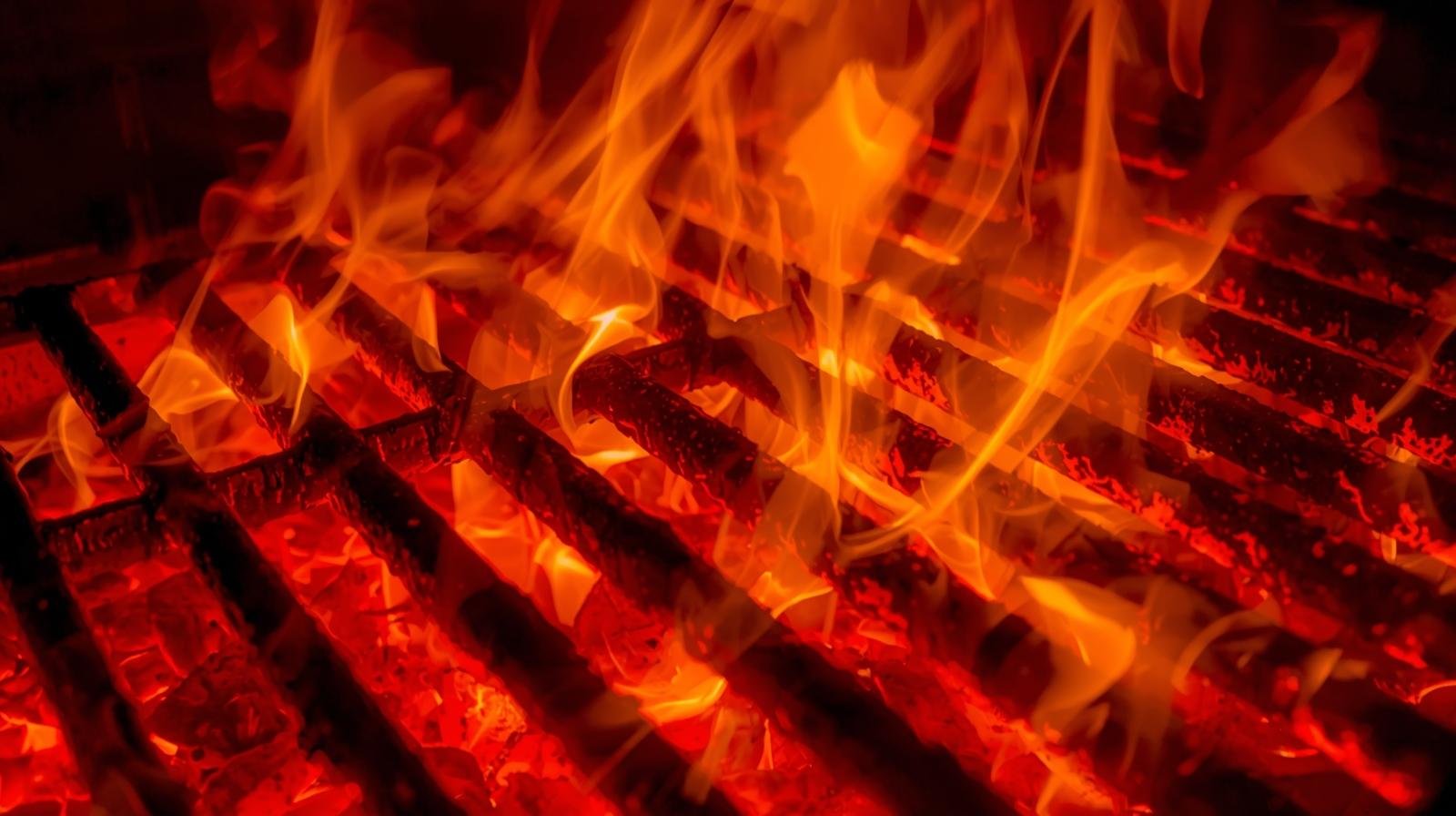 Close-up of burning wooden logs with bright orange flames on a grill.
