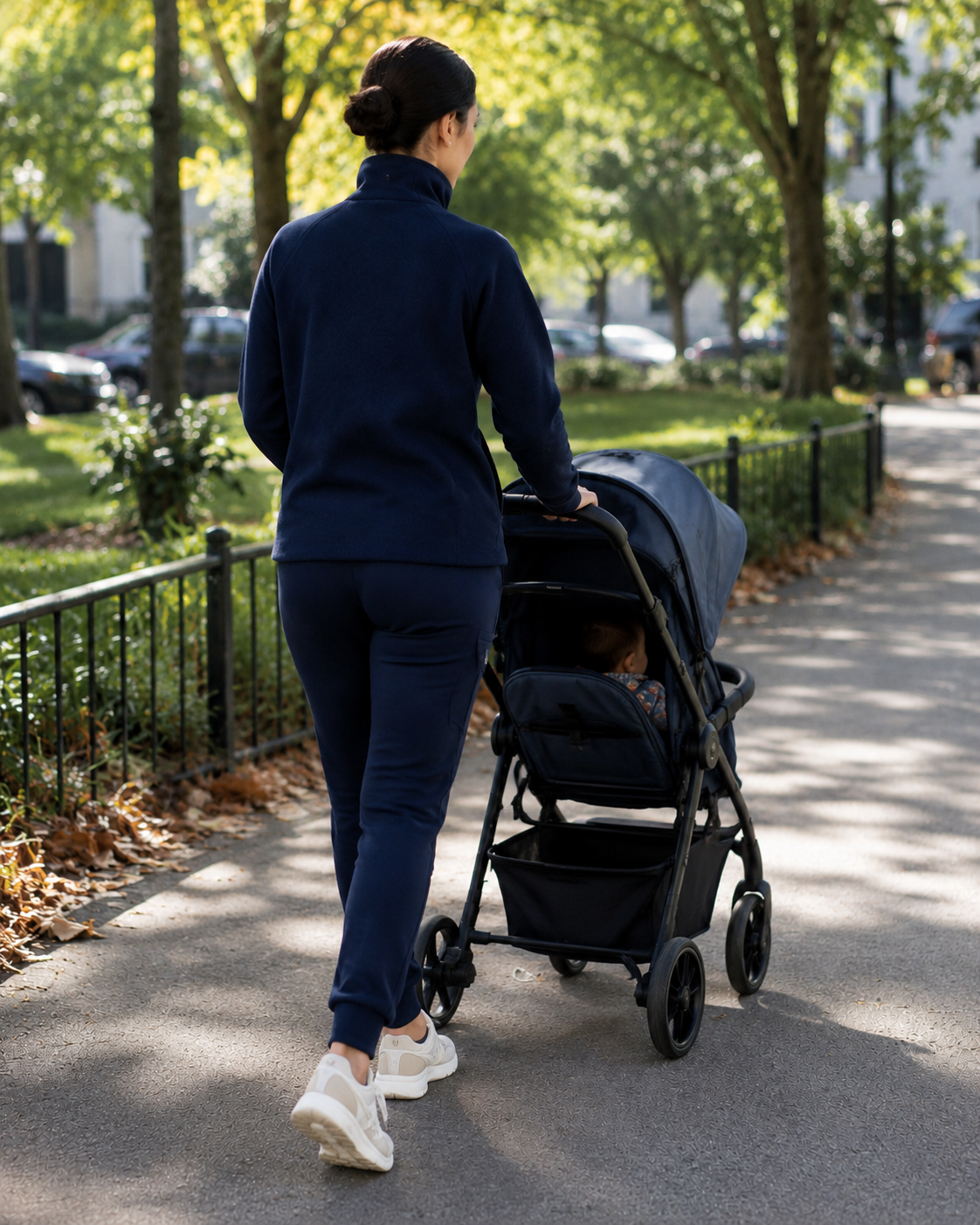 Woman pushing a stroller with a child in a park on a sunny day.