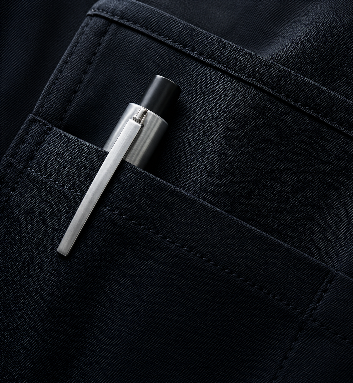 A metallic pen with a black tip in the front pocket of a dark fabric garment.