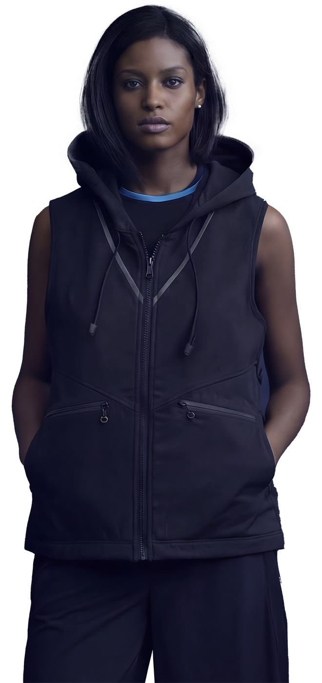 Woman with short black hair and wearing a black sleeveless hoodie with zippers and pockets, standing against a neutral background.