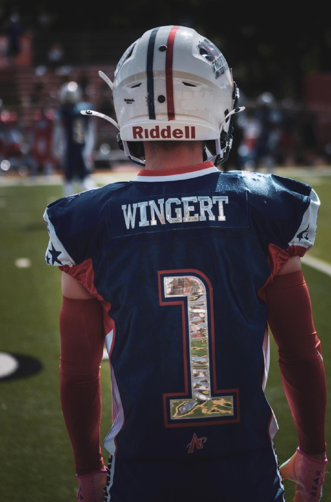 Back of an American football player wearing a navy jersey with the name WINGERT and the number 1, standing on the field during a game.
