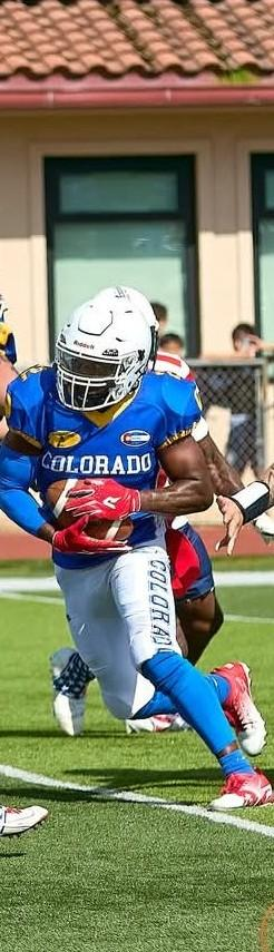 A football player in a blue Colorado jersey holding a football, running on a field during a game.
