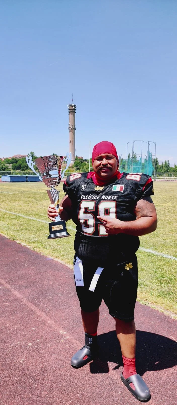 A man in football gear holding a trophy on a field, with a tall tower in the background.