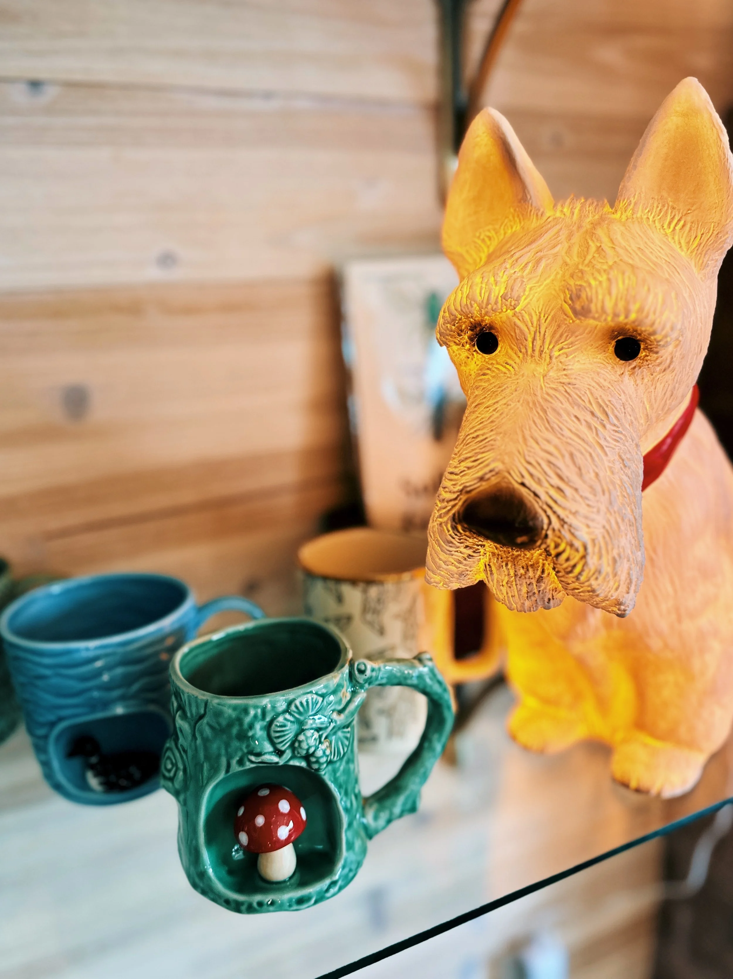 Various ceramic mugs and a decorative fox figurine on a glass shelf, with a wooden wall in the background.