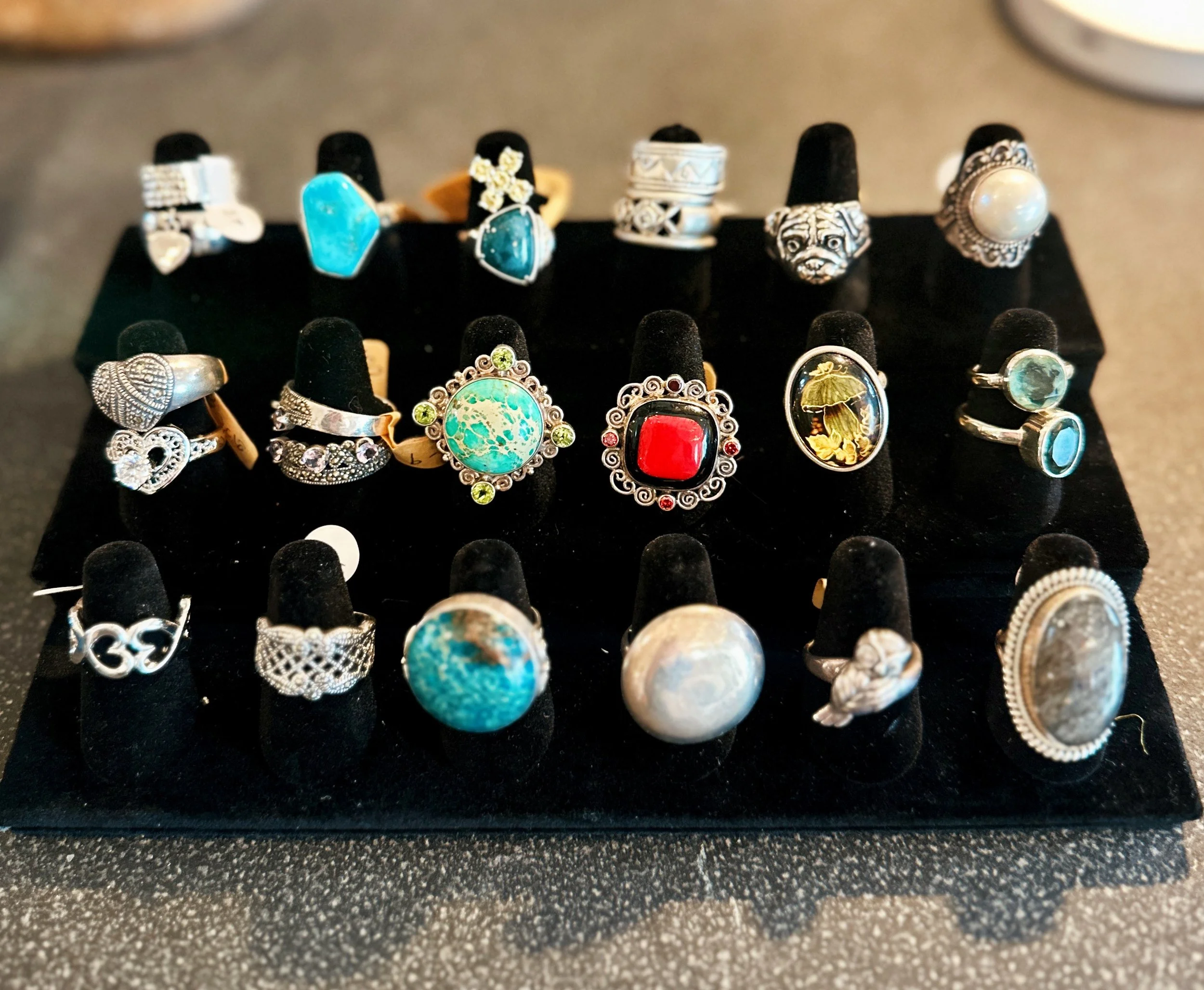 Collection of silver rings with various gemstones and designs, displayed on a black jewelry stand.
