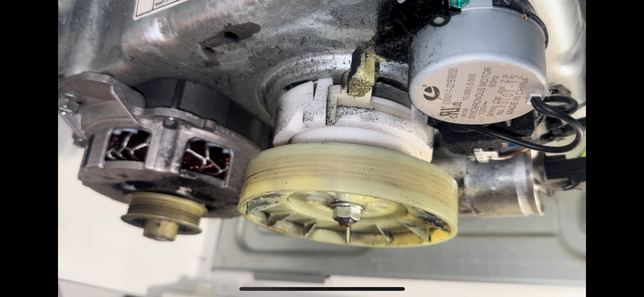Close-up of an internal part of a washing machine motor with visible pulley, wiring, and internal components.