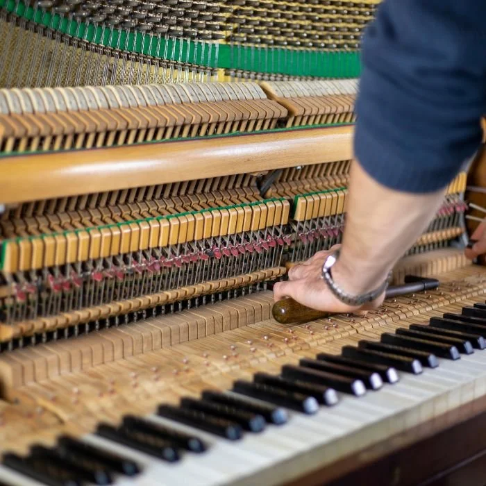 Person tuning a piano with a wrench in the internal strings and hammers