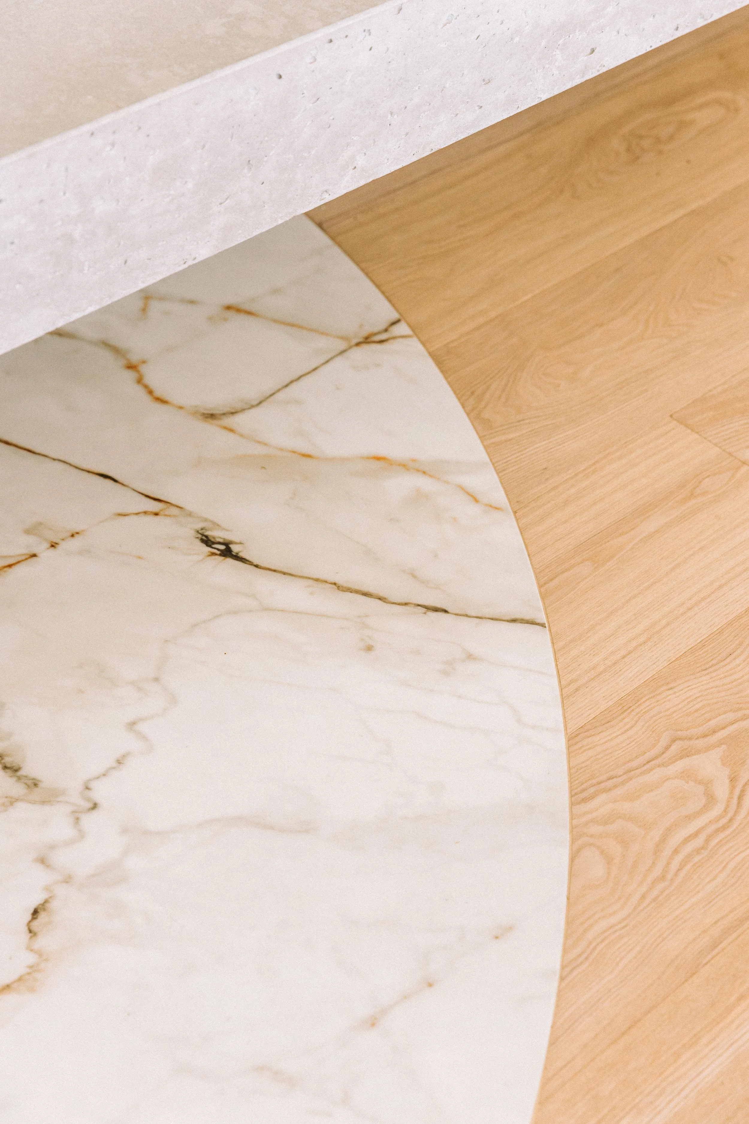 Close-up of a round table with a marble top and wooden edge, next to a beige wall.