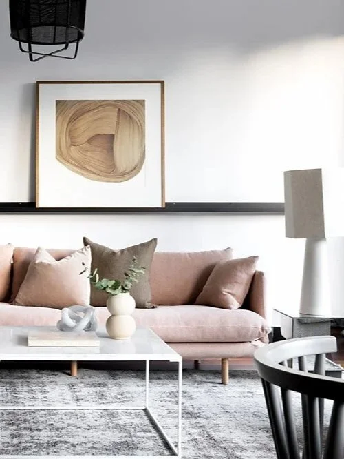 Modern living room with a pink sofa, colorful pillows, a white coffee table with decorative items, abstract wall art, and a floor lamp.