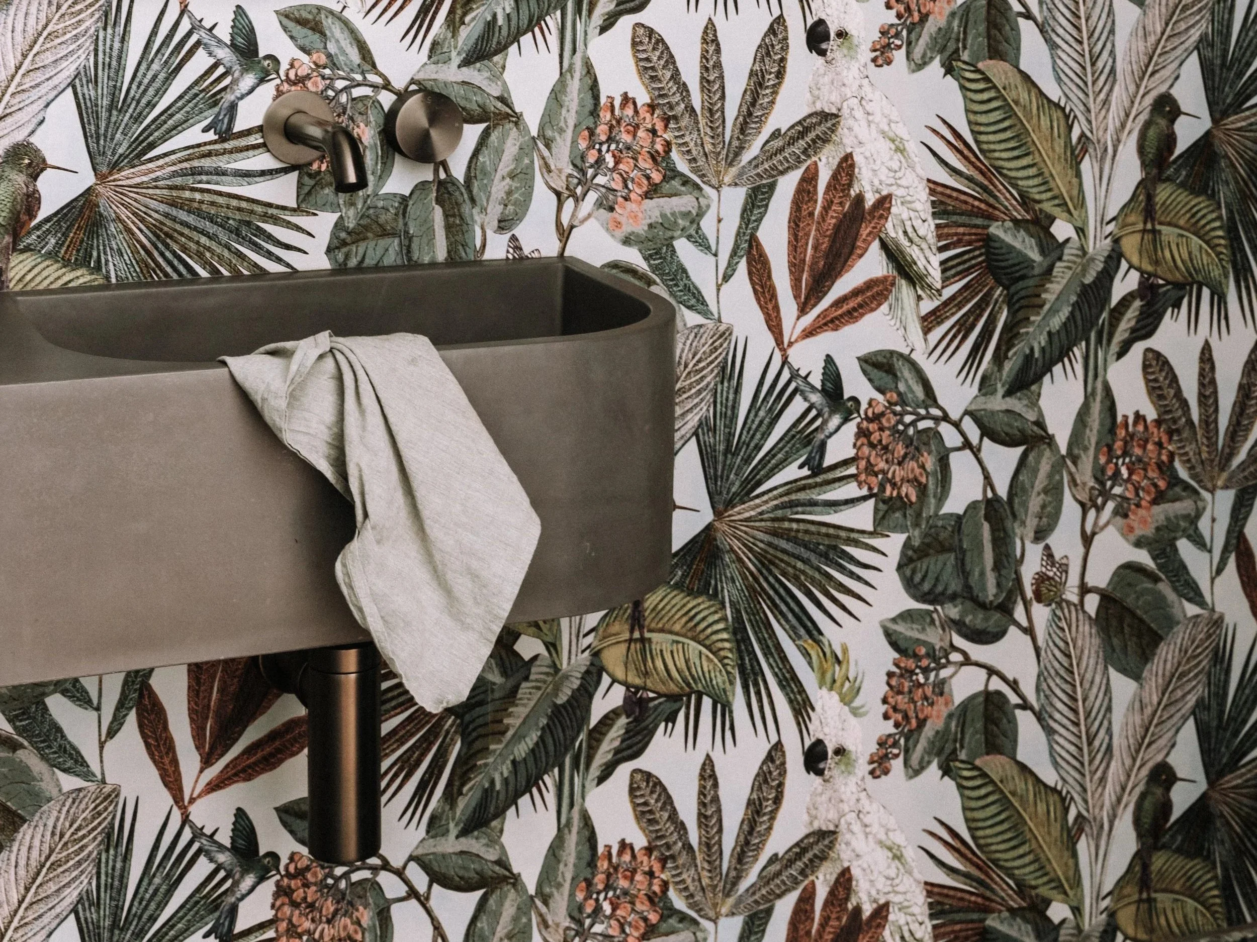 Bathroom with a dark gray sink, a towel draped over the side, and a wall decorated with tropical leaf and bird wallpaper.