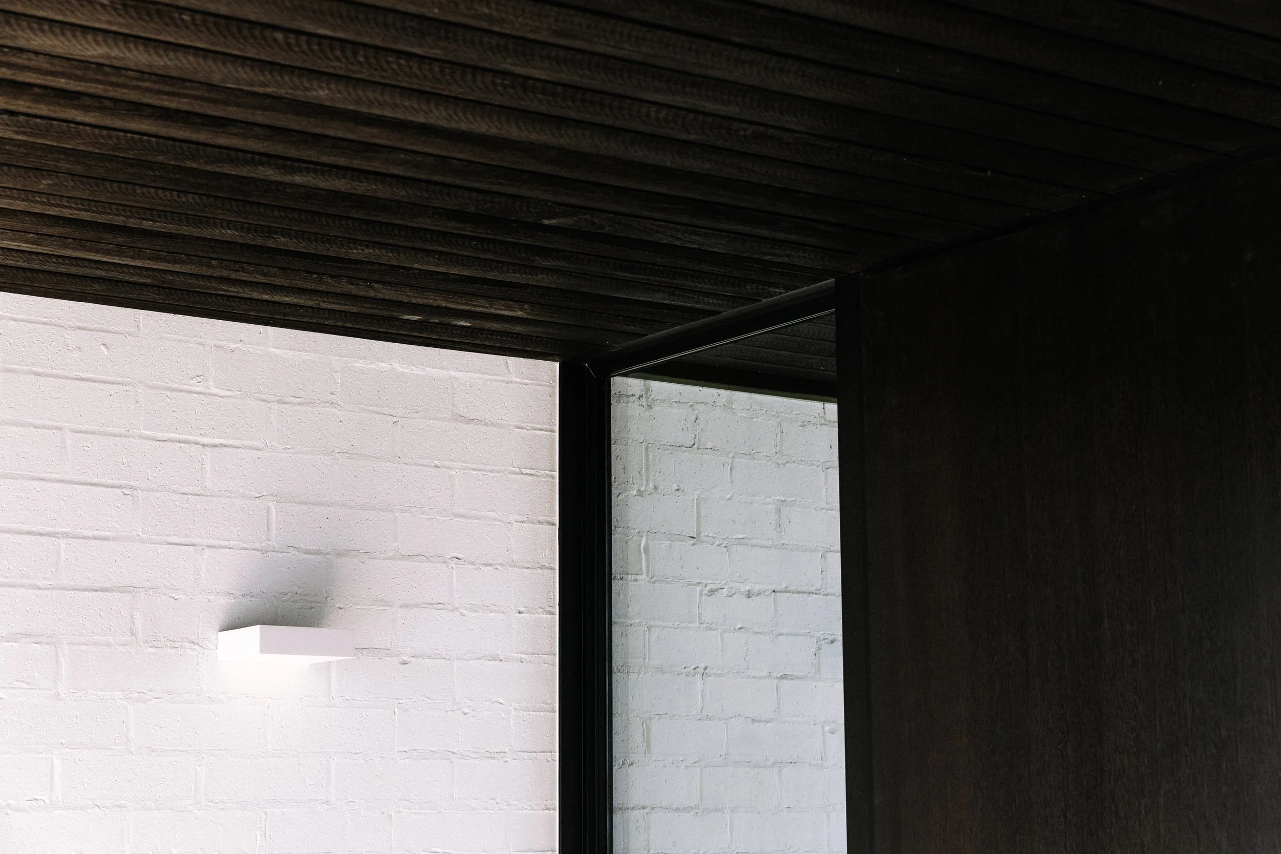 Close-up of a black wooden ceiling and wall, with a white brick wall in the background.