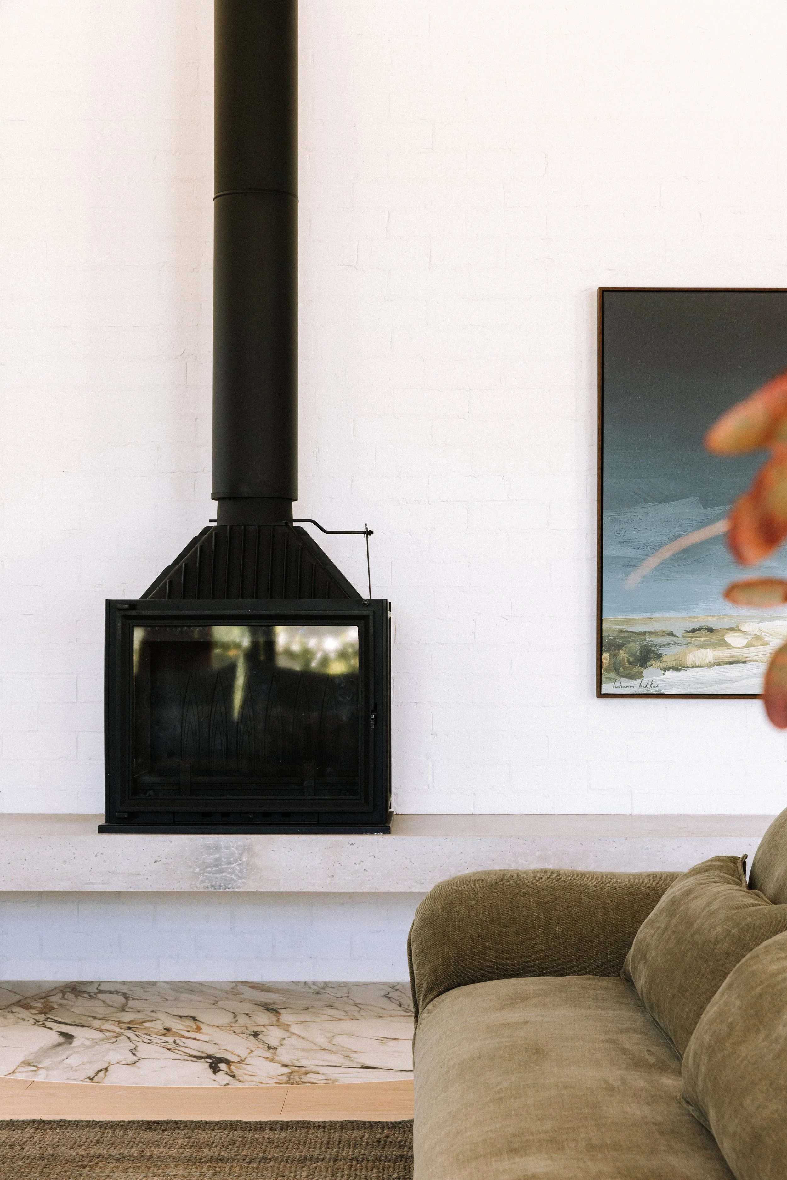 Living room with a black fireplace on a white brick wall, a framed landscape painting, and part of a green sofa.