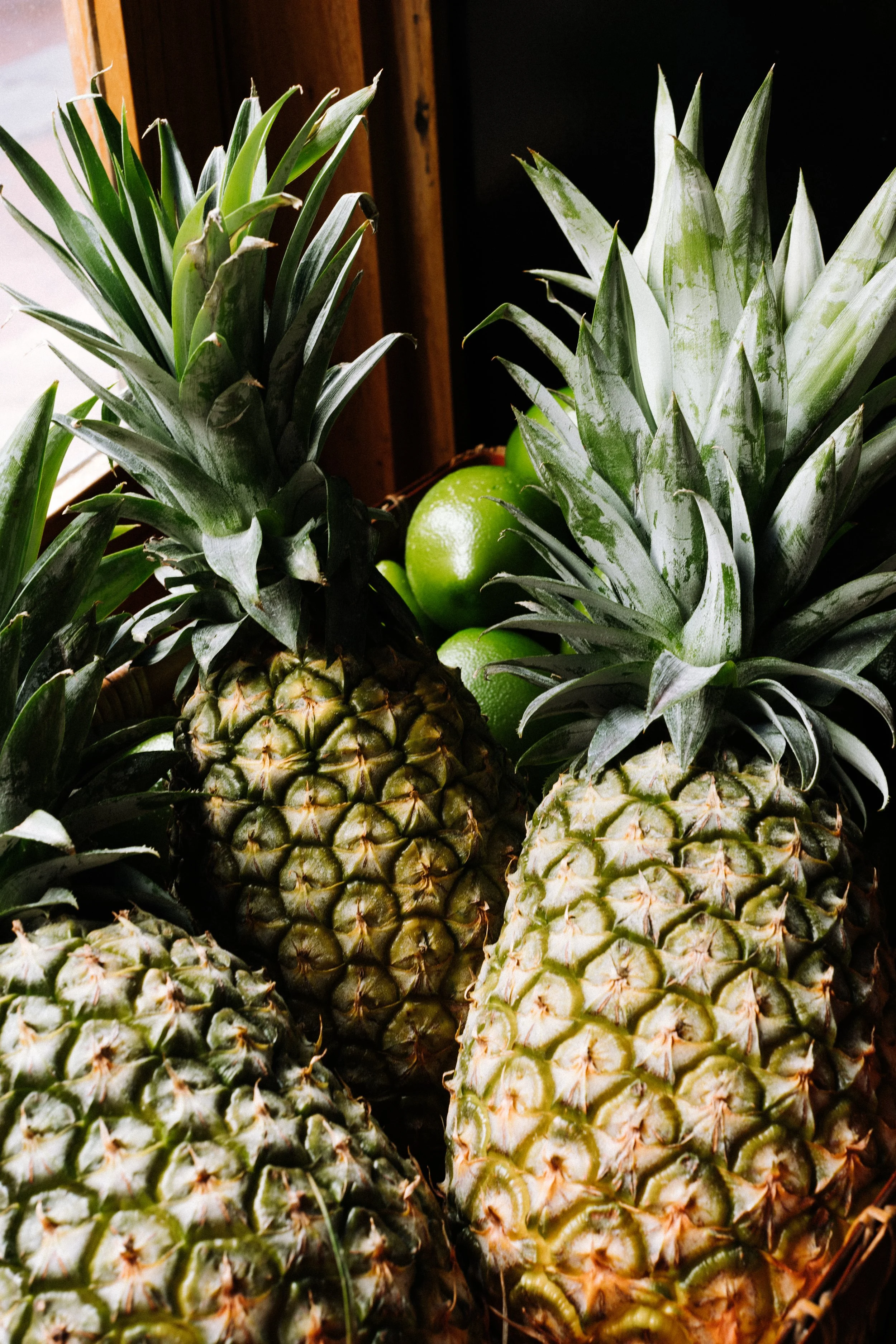 Group of pineapples with green leaves and a couple of green limes in the background.