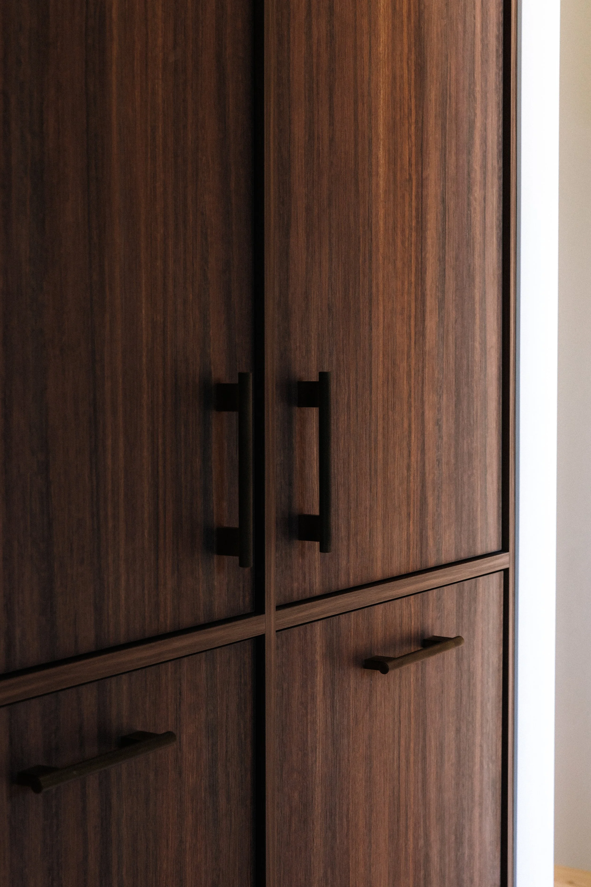 Close-up of dark wood cabinet doors with black handles, next to a white wall.