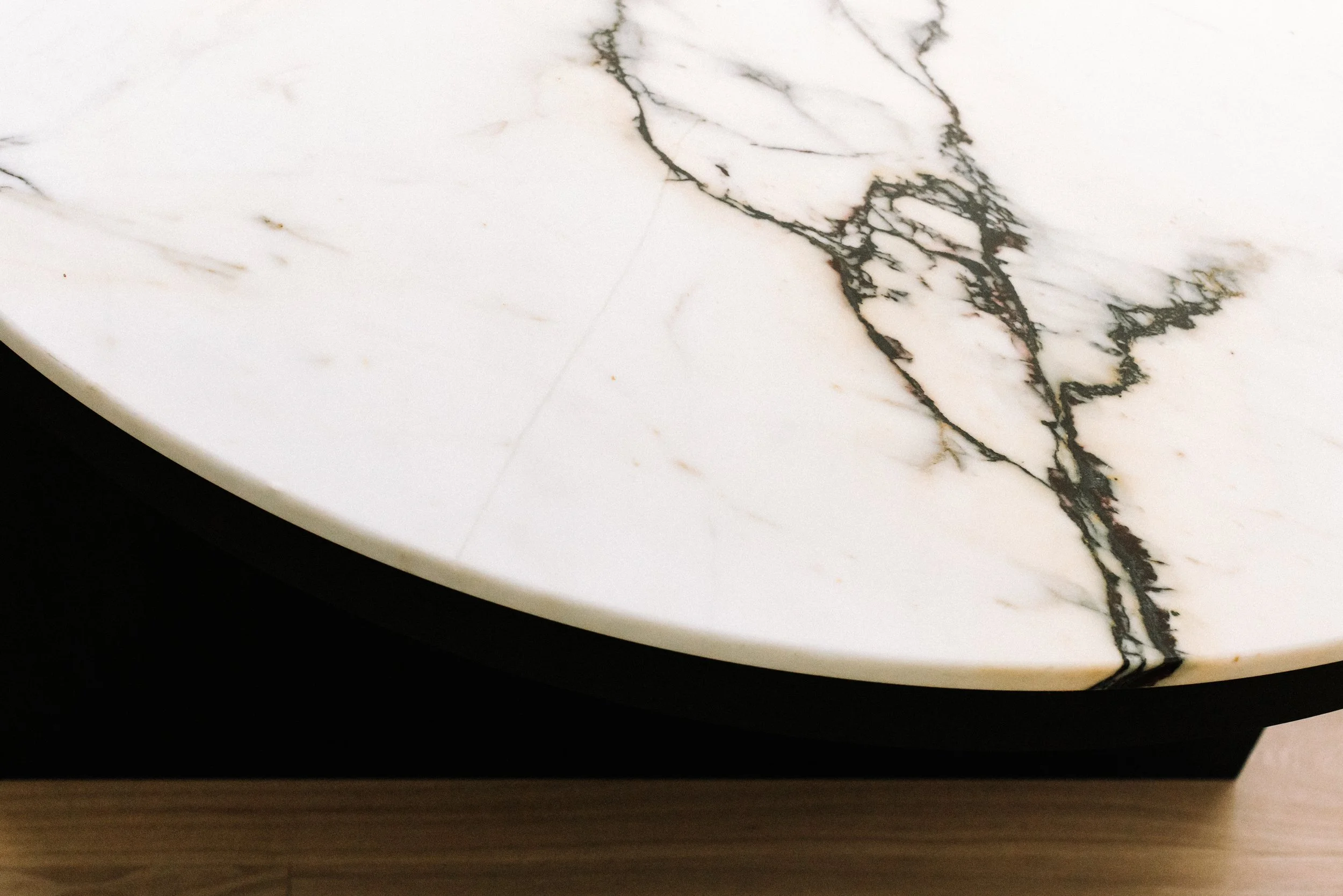Close-up of a white marble surface with black veins, on a wooden table edge.