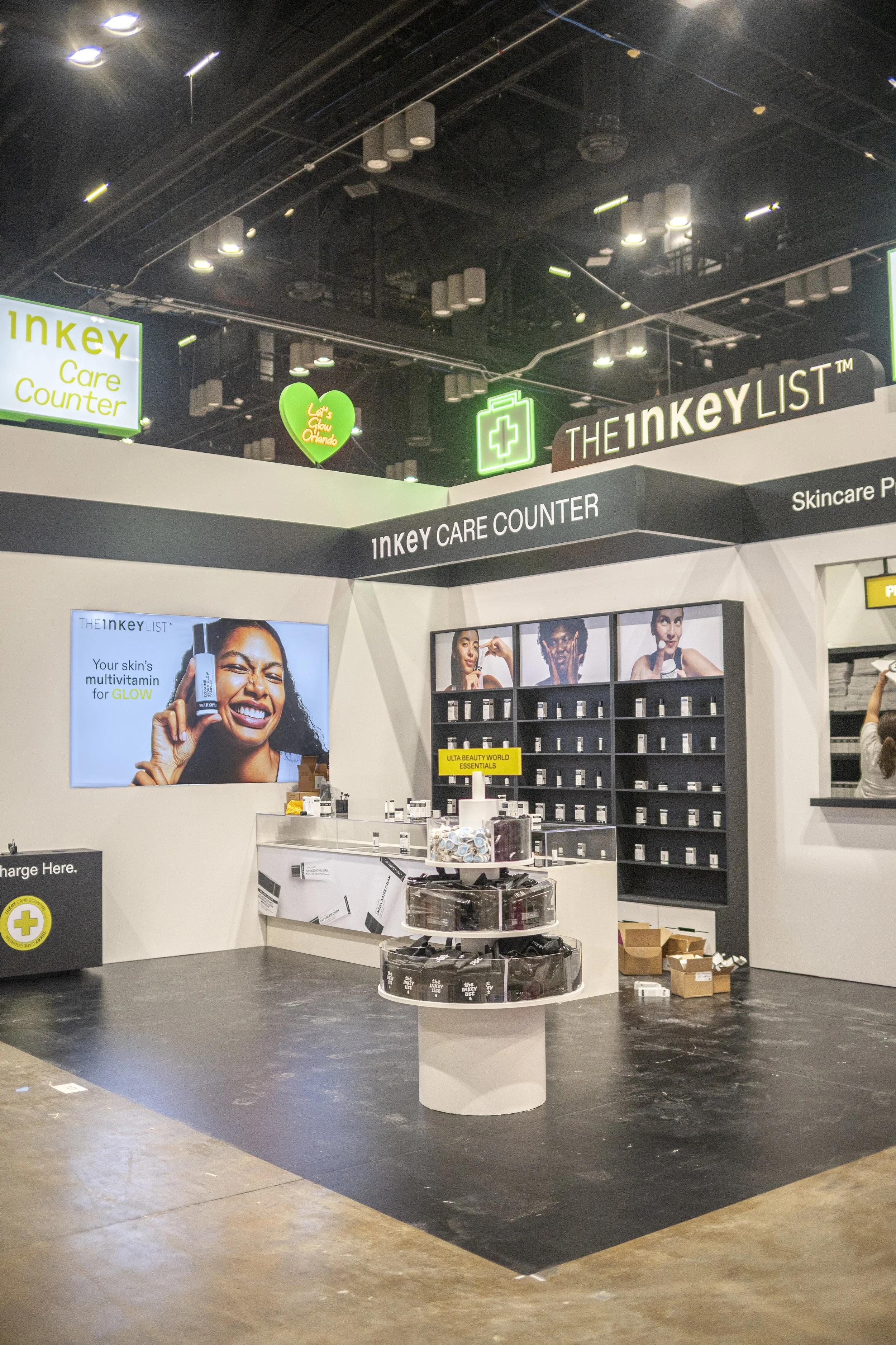 An indoor retail display for skincare products called THE INKEY LIST. The display features signage, a large digital screen with a smiling woman holding a skincare product, shelves with various skincare items, and promotional posters.