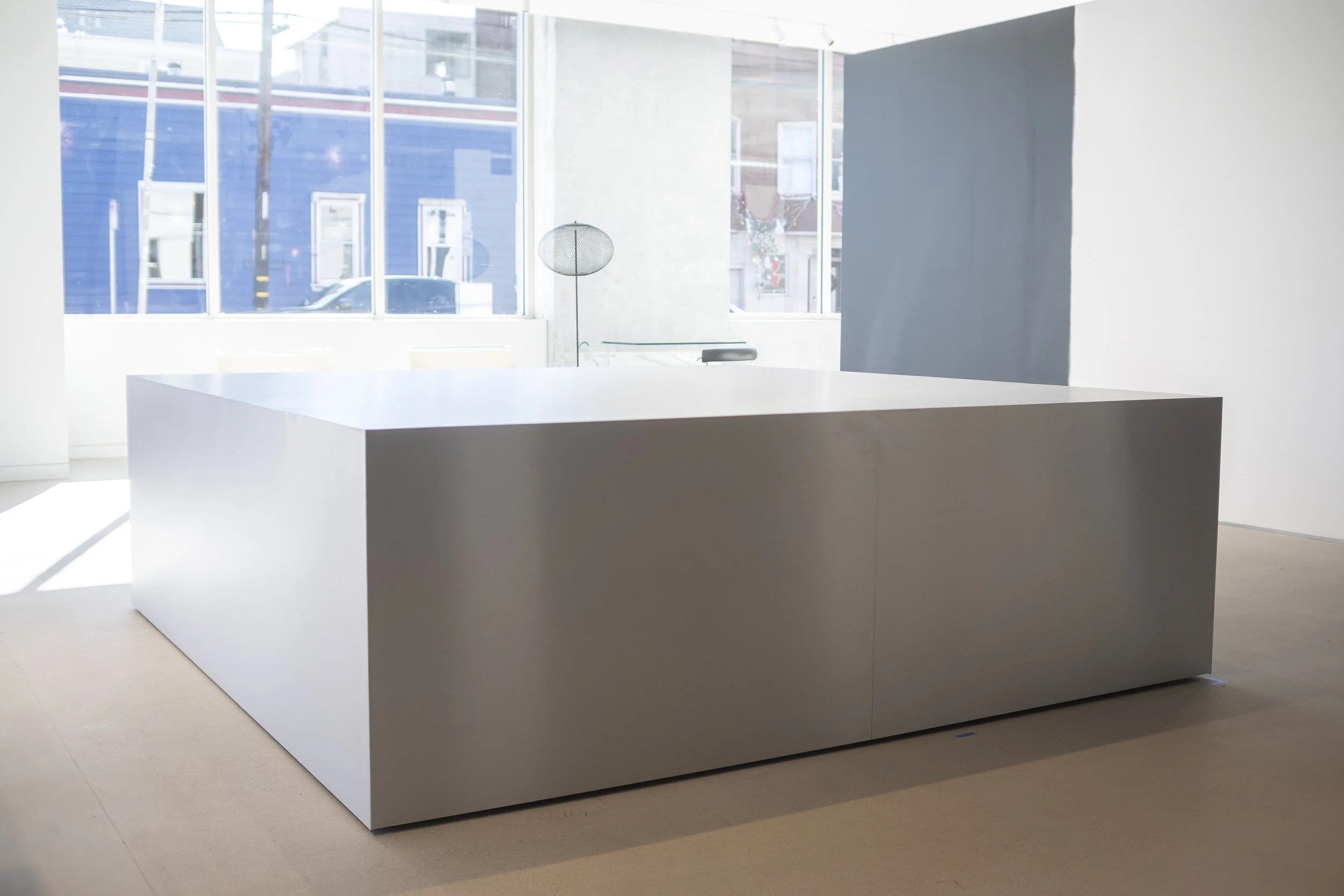 A modern, minimalist white examination table or counter in a bright room with large windows, allowing natural light to fill the space.