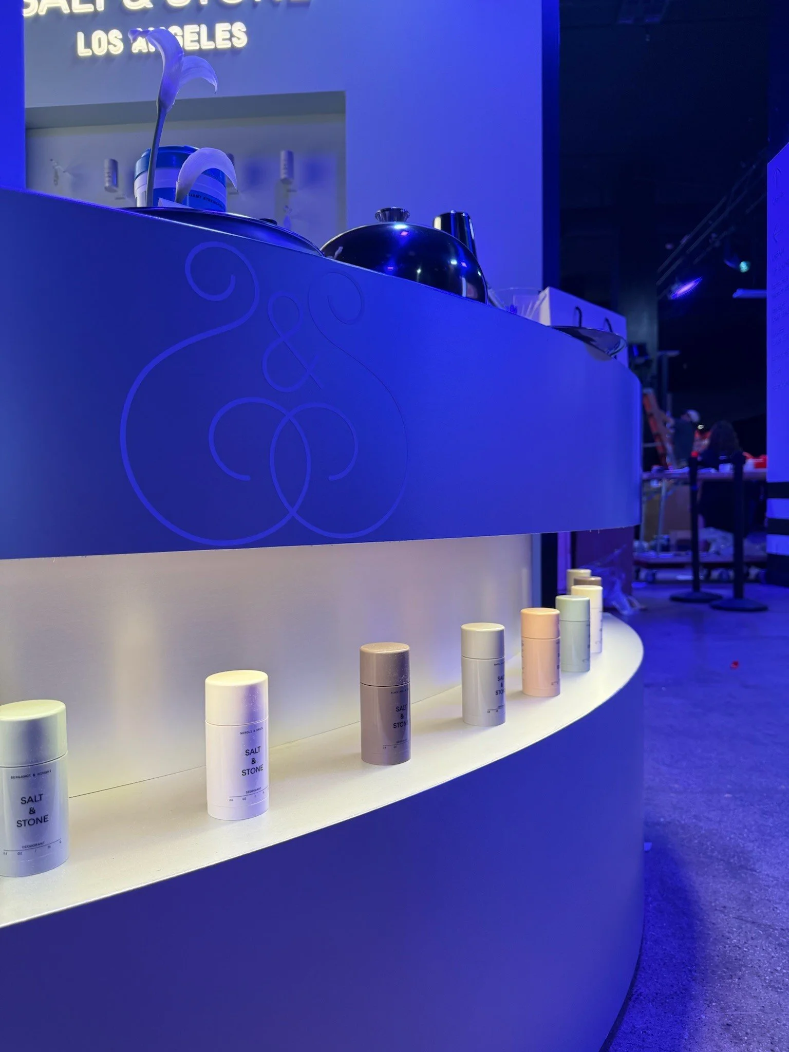A display of salt and stone products in white bottles on a white shelf, with a dark blue background and some people in the distance.